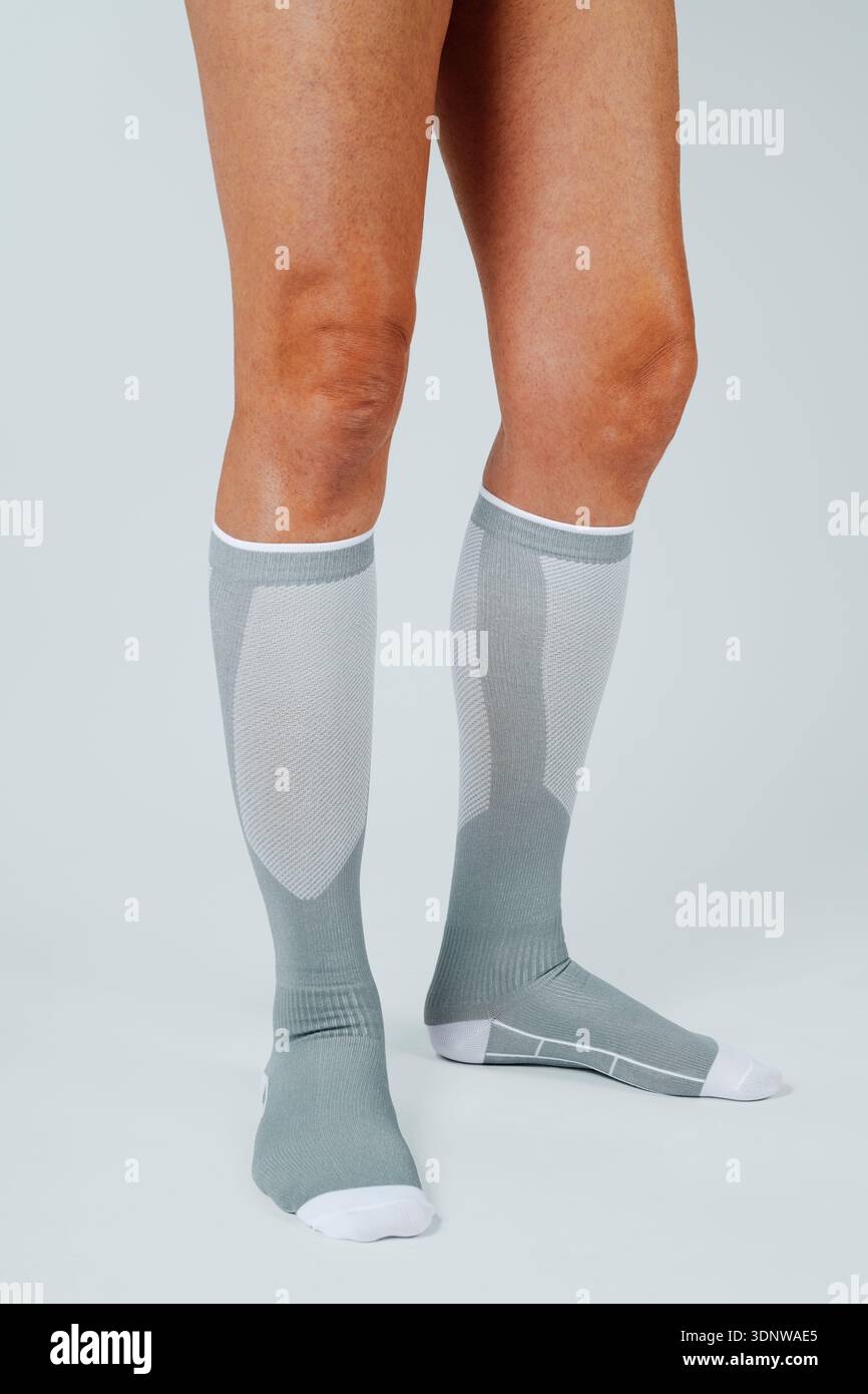 la parte inferiore delle gambe di un uomo che indossa calzini di compressione grigi che si estendono fino al ginocchio, progettati per migliorare la circolazione e fornire supporto muscolare su una b grigia Foto Stock
