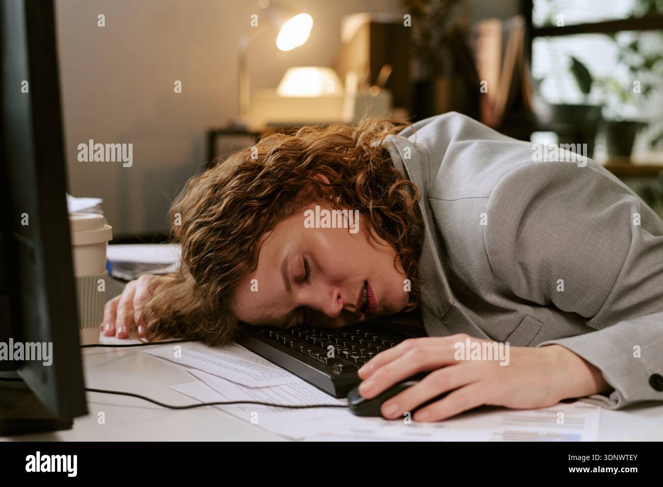 Giovane donna che dorme sulla tastiera mentre lavora in ufficio Foto Stock