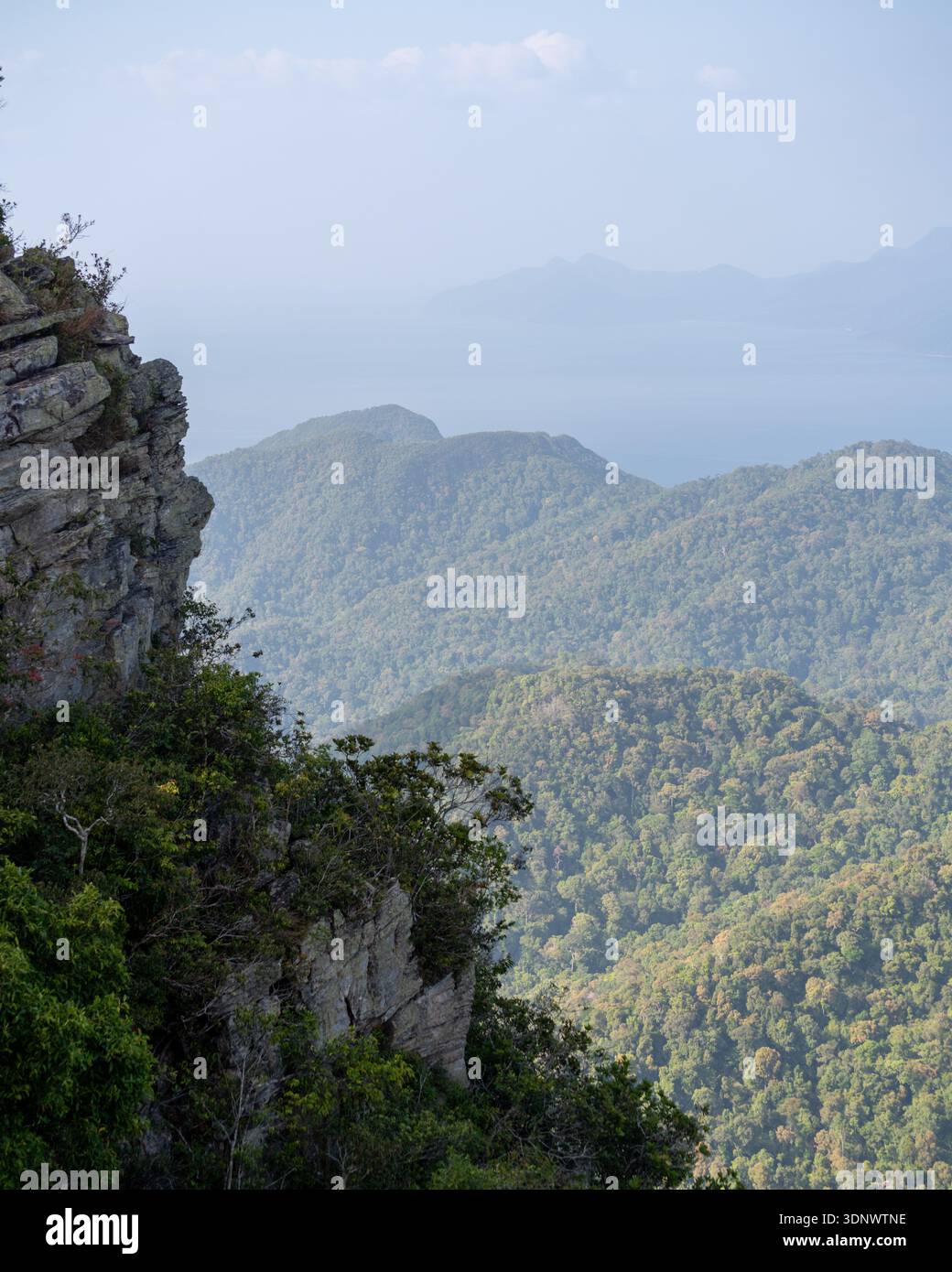 Una spettacolare scogliera si affaccia su montagne ondulate e ricoperte di foreste con una vista morbida e nebulosa verso il lontano mare di Langkawi, Malesia. Foto Stock