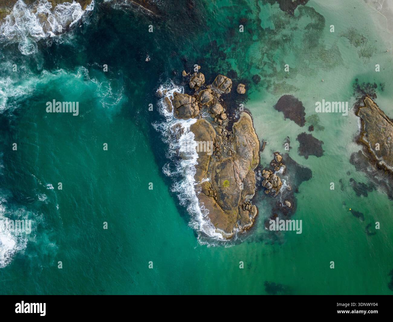 Una scena costiera sopraelevata mostra le onde che si infrangono su una barriera corallina rocciosa circondata da profonde acque blu e turchesi con motivi subacquei visibili. Foto Stock