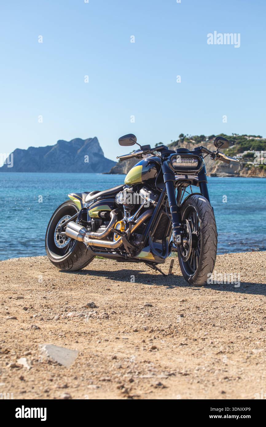 Un'elegante motocicletta personalizzata poggia su una spiaggia sabbiosa, affacciata su un mare tranquillo sotto un cielo azzurro. Perfetto per viaggi avventurosi, questo veicolo combinato Foto Stock