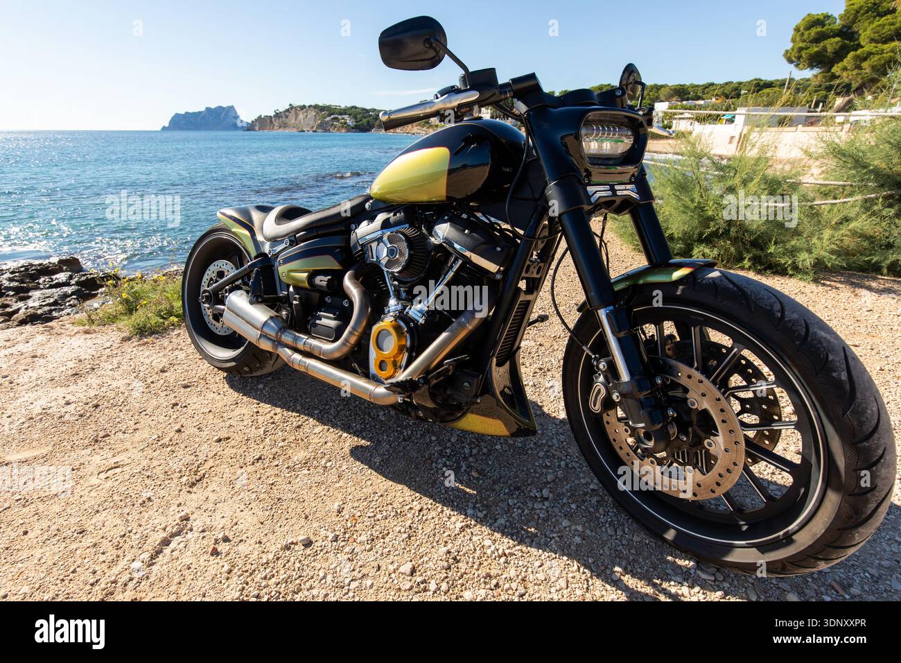 Un'elegante motocicletta personalizzata parcheggiata su un sentiero di ghiaia sulla spiaggia, con uno splendido sfondo oceanico. Questo veicolo incarna lo spirito di avventura e libertà, Re Foto Stock