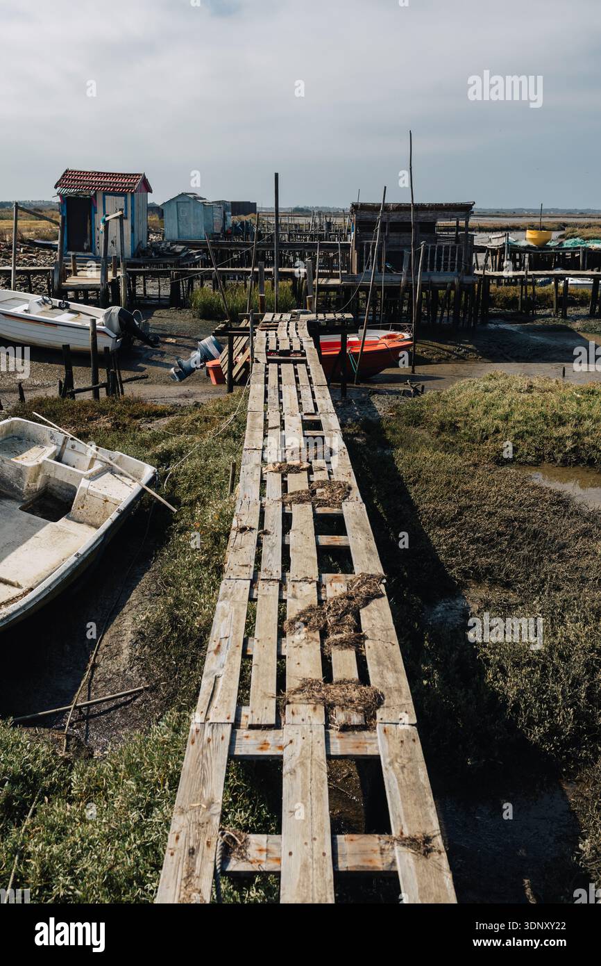 Immagine di un molo abbandonato che si estende in un bacino di mare asciutto, circondato da barche a terra e strutture in legno intemperie, catturando una scena suggestiva Foto Stock