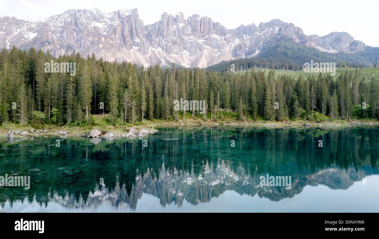 Veduta aerea del Lago di Carezza che riflette le vette torreggianti del massiccio del Latemar. Circondato da foreste sempreverdi, questo idilliaco scenario alpino captiva Foto Stock