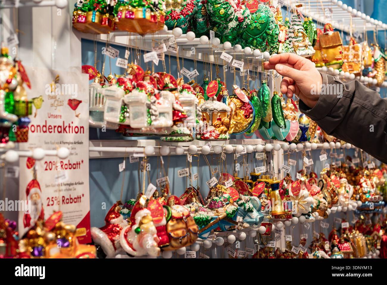 Cliente che esamina gli ornamenti colorati in vetro presso uno stand di un mercato natalizio che presenta una promozione speciale Foto Stock