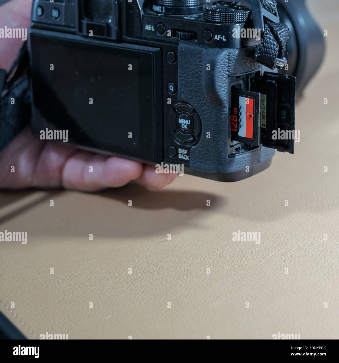 Una mano inserisce una scheda SD da 128 GB in una fotocamera digitale, pronta per l'acquisizione di foto e video. Foto Stock