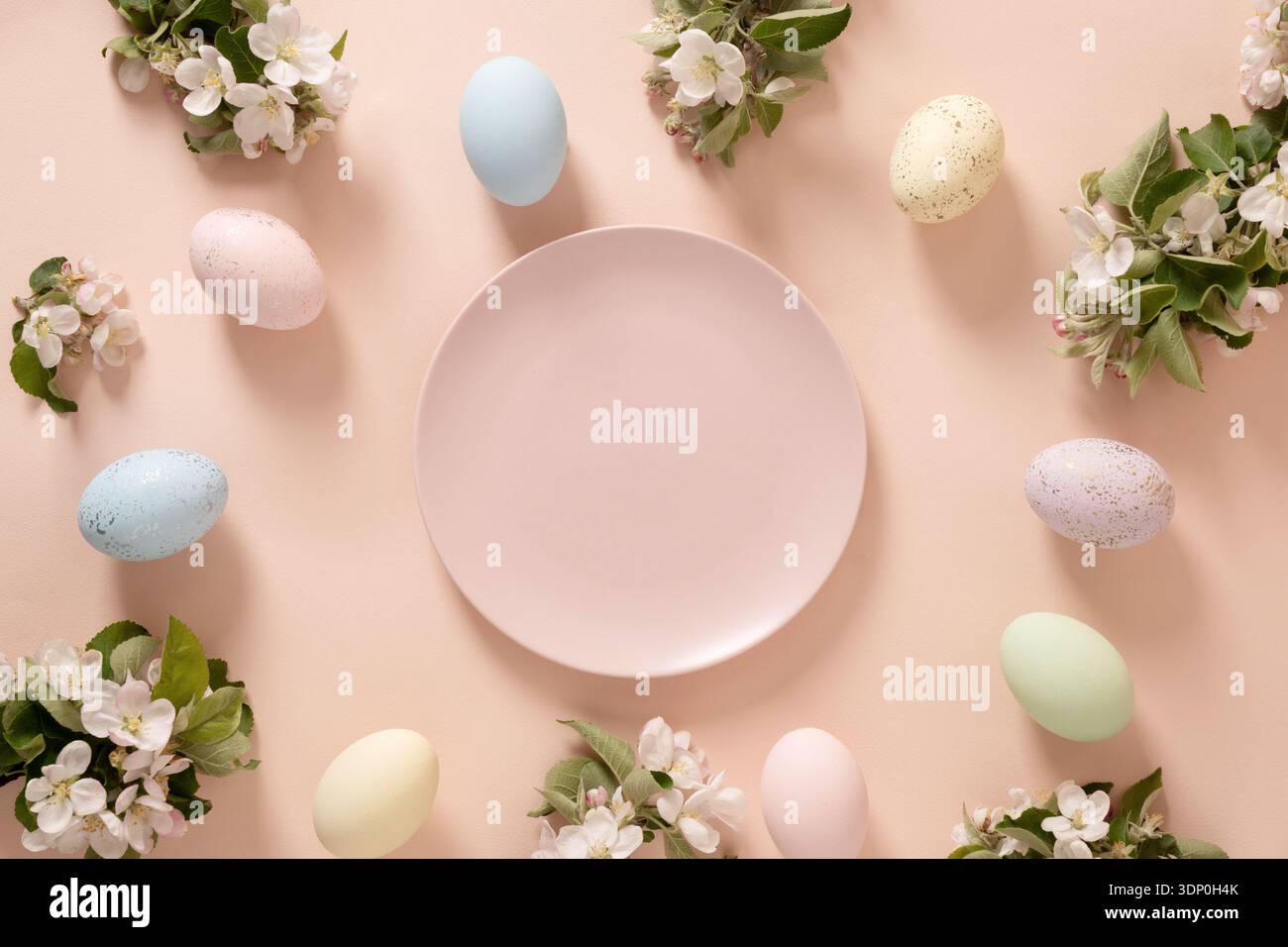 Scena pasquale con uova pastello, rami in fiore e piatto vuoto al centro su un morbido sfondo pesca per un design natalizio. Vista dall'alto Foto Stock