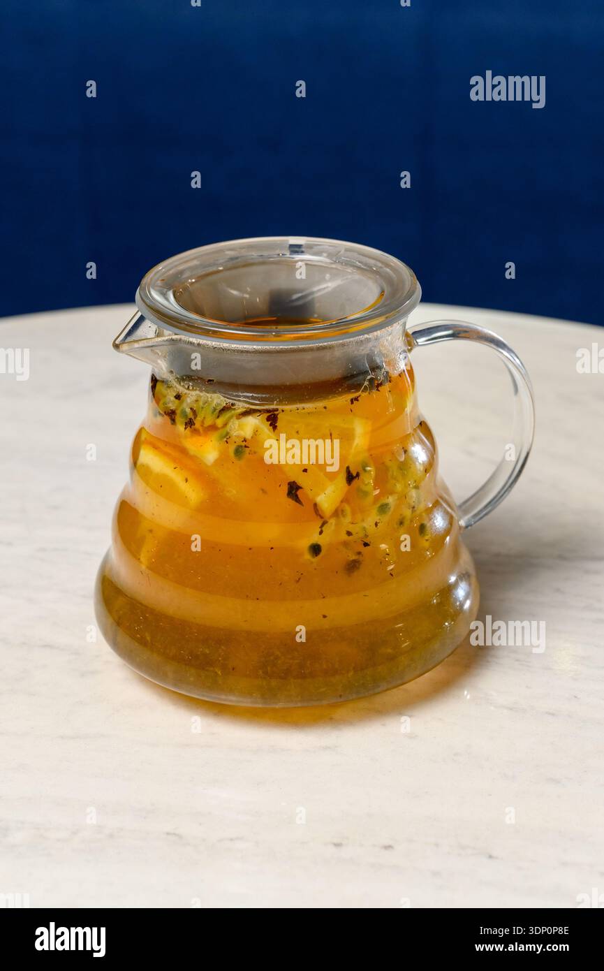 Teiera di vetro con tè all'arancia e al frutto della passione. Una teiera trasparente con una bevanda calda e fette di agrumi in una caffetteria Foto Stock