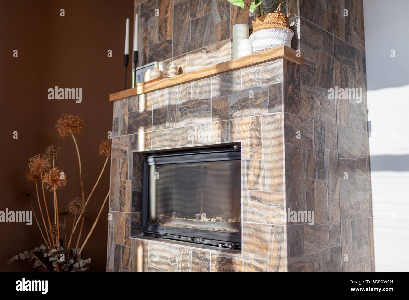 Caminetto ricoperto di piastrelle che imitano la consistenza della pietra. Mantel decorato con candele e piante. Interno del soggiorno Foto Stock