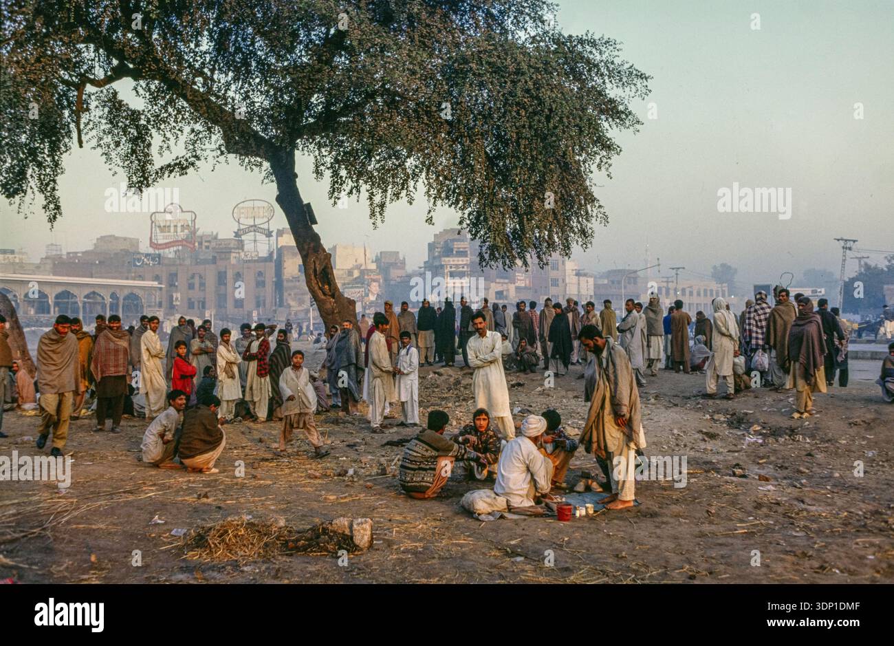 Gli uomini si riuniscono in un punto del sole mattutino per riscaldarsi, mentre aspettano di essere assunti come operai quotidiani, a Rawalpindi, Pakistan Foto Stock