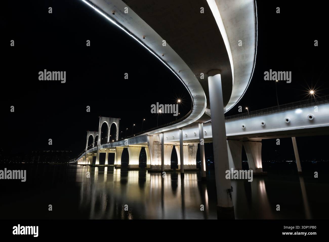 Ampie curve in cemento della rampa di accesso illuminata del ponte Sai Van di notte, che mostrano gli archi principali del ponte e i riflessi sull'acqua, Macao. Foto Stock