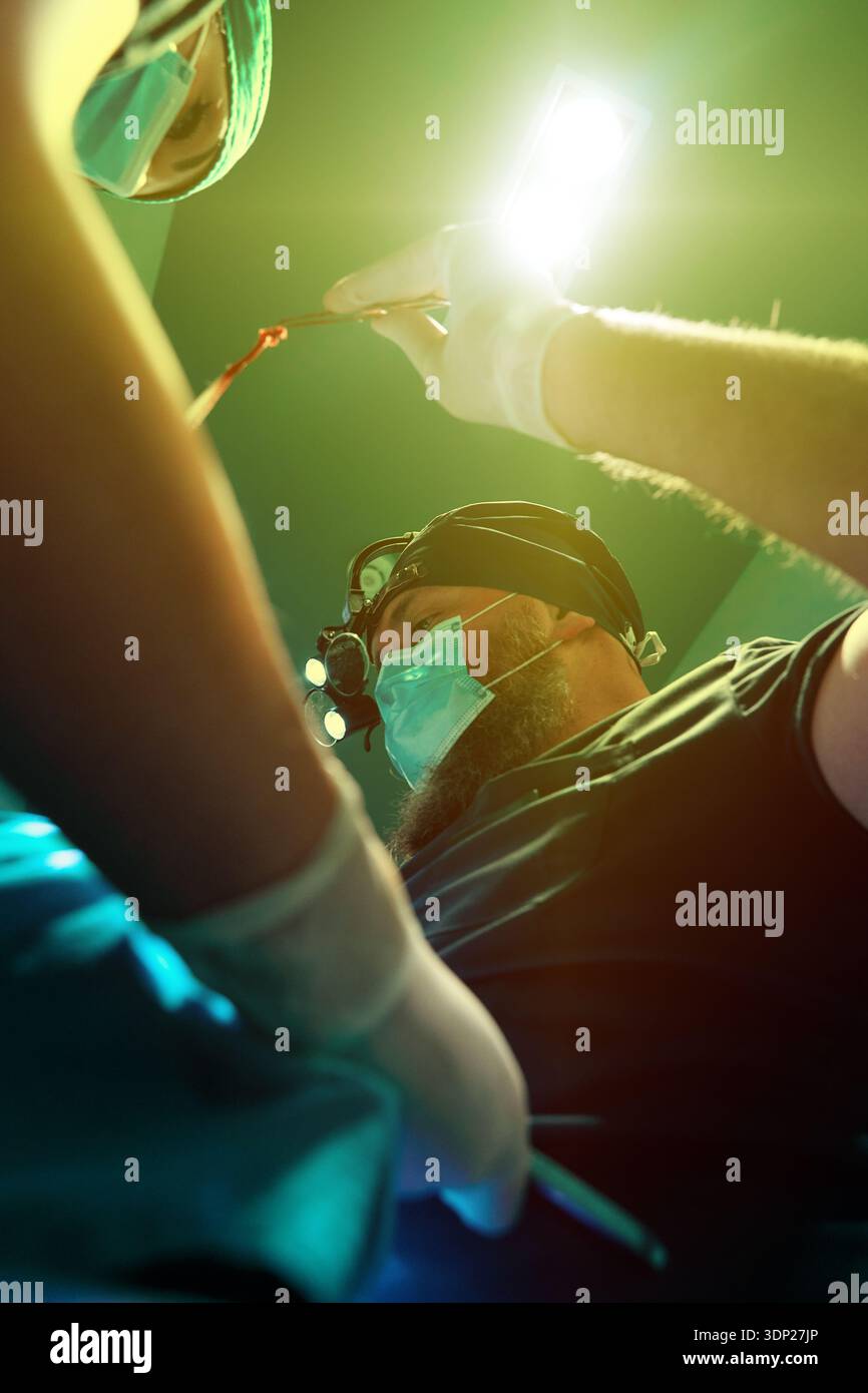 I chirurghi in sala operatoria eseguono procedure precise sotto luce chirurgica brillante, maschera e focalizzata Foto Stock