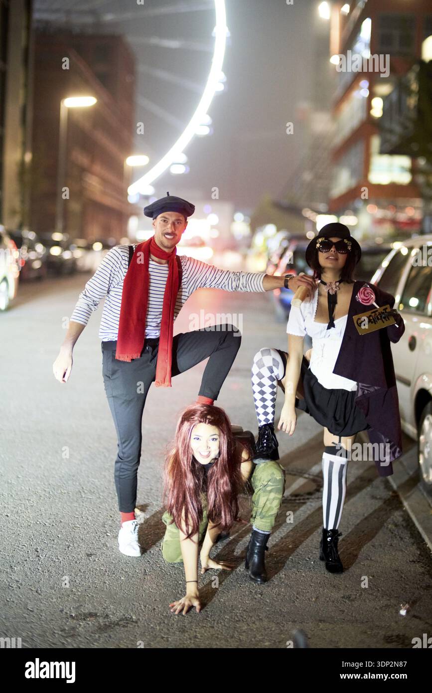 Dominanza gerarchica di tre amici in costume che si posa giocosamente sotto le luci della città in una strada urbana di notte, vita notturna, atteggiamento di sottomissione simile a un cane Foto Stock