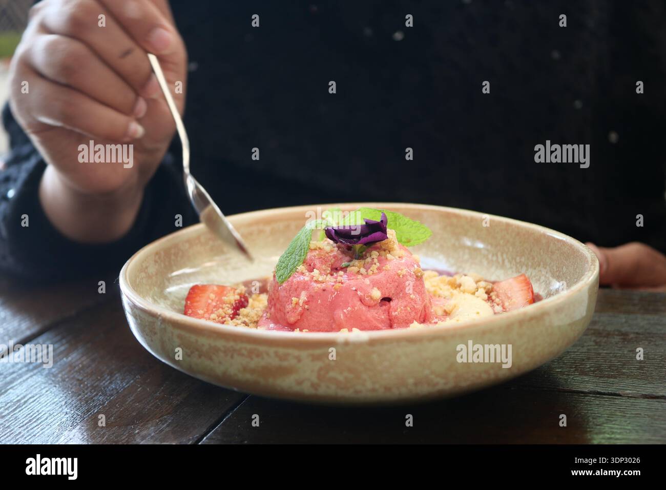 Una persona assaggia un dessert con gelato, frutta e contorno in un caffè Foto Stock