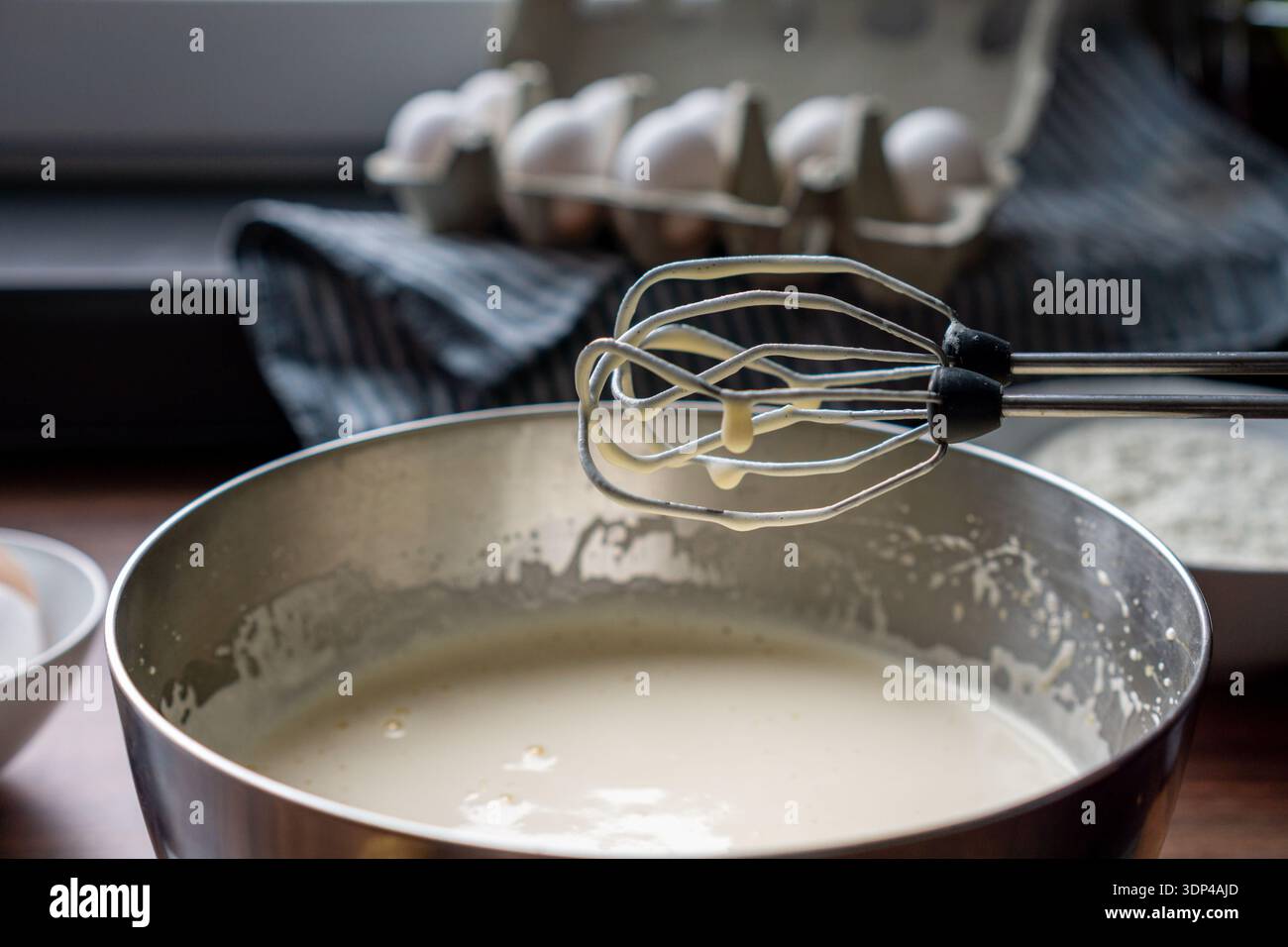 Le fruste del mixer elettrico coperte dall'impasto per torte vengono sollevate sopra un recipiente di miscelazione in metallo. Foto Stock