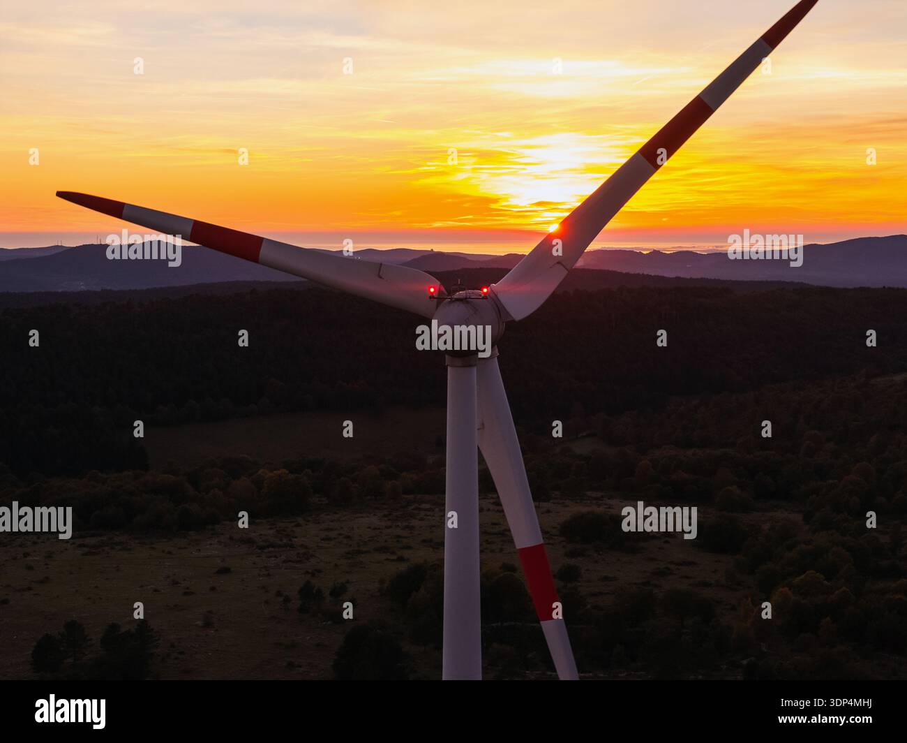 Vista aerea di una turbina eolica durante il tramonto con luce calda sul paesaggio e sulle montagne. La scena mostra le risorse energetiche rinnovabili. Foto Stock