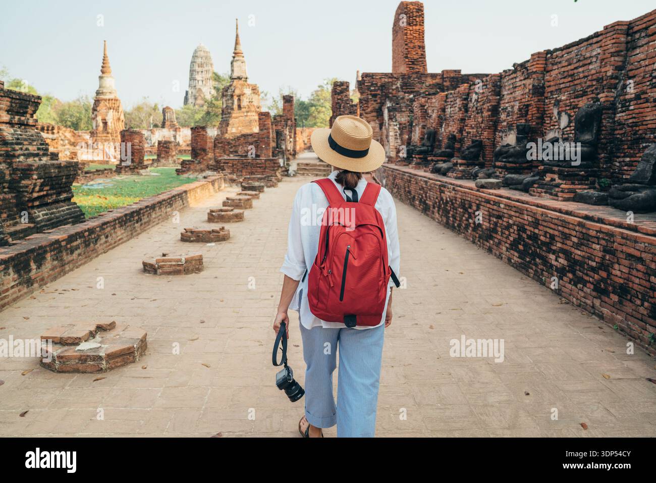 Giovane donna turistica a piedi con fotocamera compatta attraverso Ayutthaya Wat Phra RAM antiche rovine in Thailandia. Storia, turismo, concetto turistico. Foto Stock