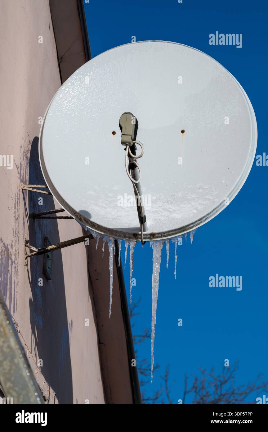 Parabola satellitare congelata con ghiaccioli lunghi in un edificio residenziale Foto Stock