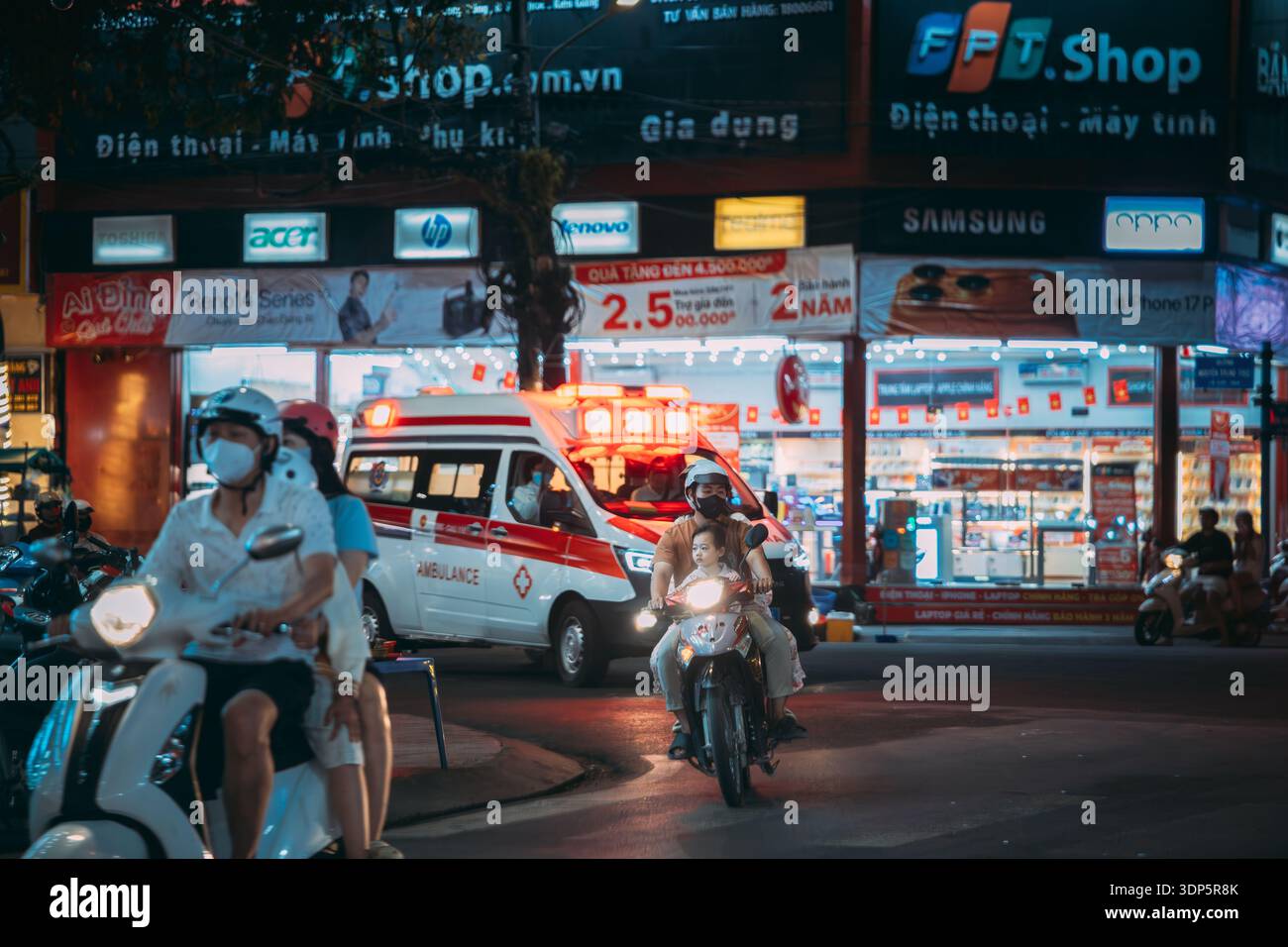 Ambulanza con luci di emergenza che guidano attraverso il traffico di scooter affollato di notte Foto Stock