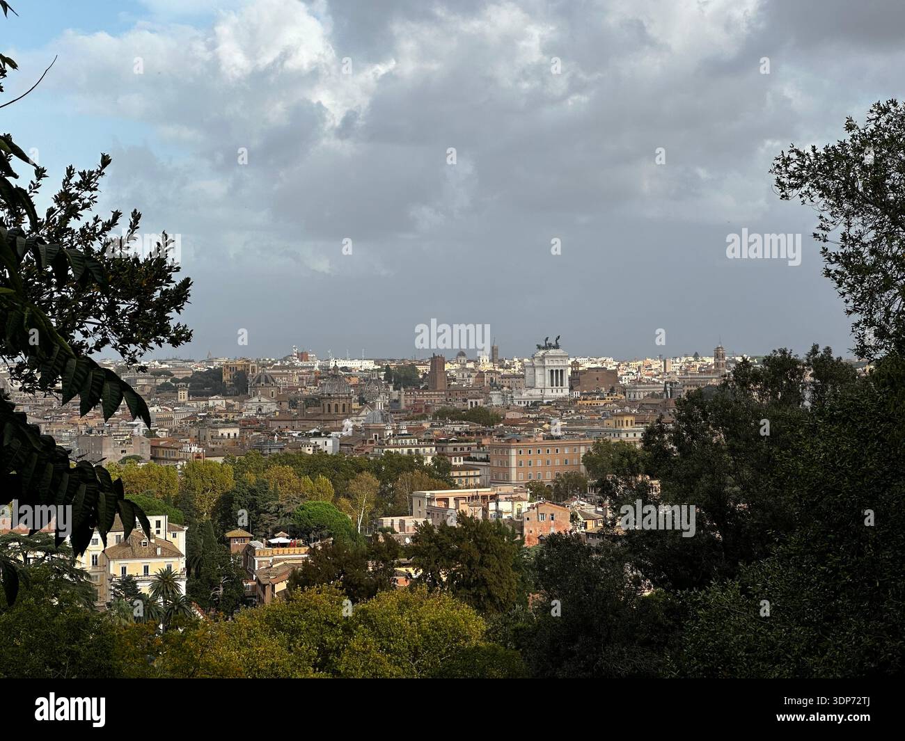 Un pittoresco paesaggio urbano di Roma con un cielo blu nuvoloso, caratterizzato da un mix di edifici moderni e vegetazione. La scena cattura l'essenza della vita urbana Foto Stock