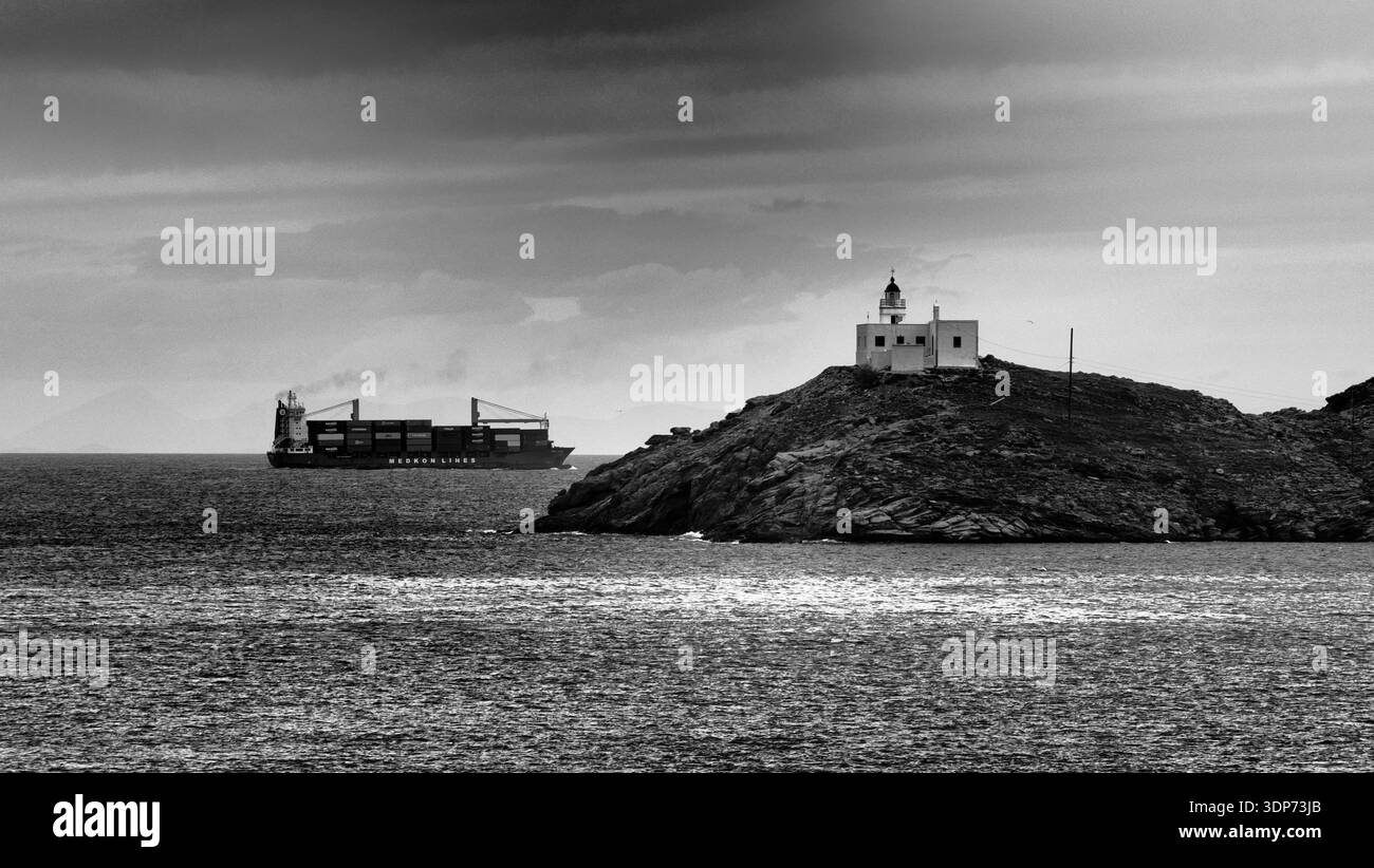 Mare bianco e nero di una nave portacontainer che naviga nel Mar Egeo vicino al faro di Korissia sull'isola di Kea, Cicladi, Grecia. L'isolotto roccioso W Foto Stock