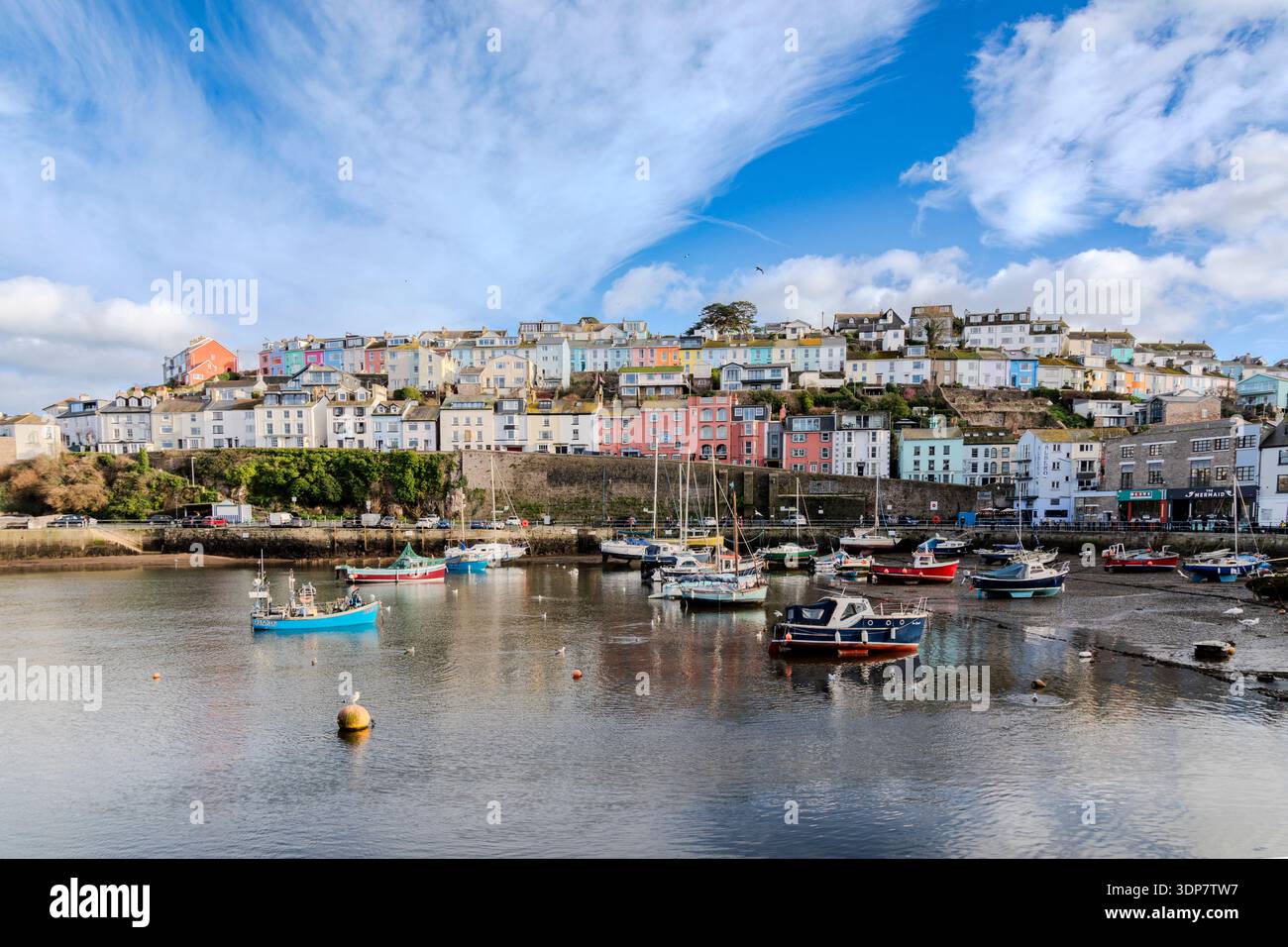 Colina colorata di Brixham, con barche ormeggiate con la bassa marea, sotto un cielo azzurro con nuvole sottili. Foto Stock
