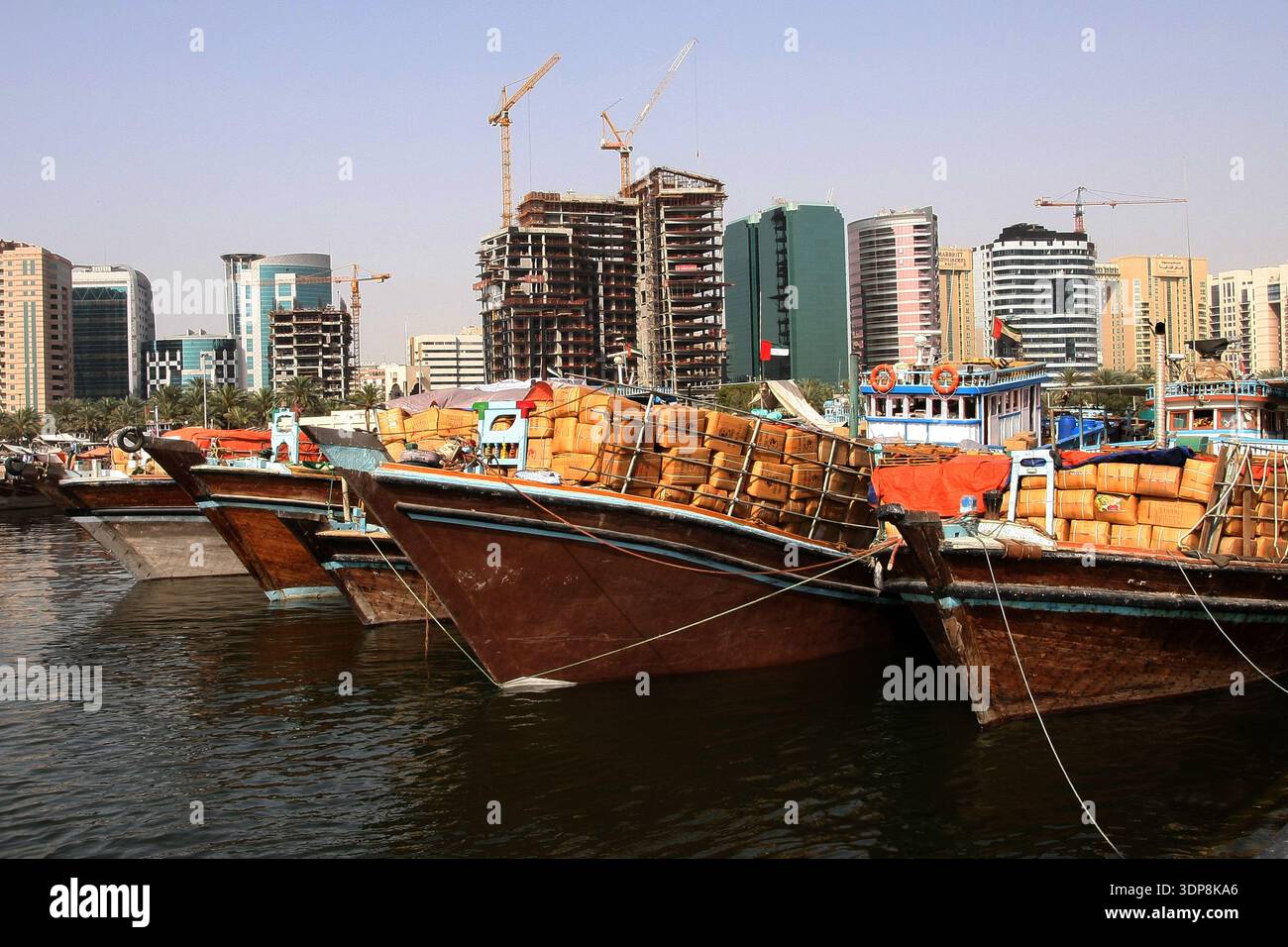 Tradizionali barche da carico in legno (dhow) caricate di merci ormeggiate al Dubai Creek davanti allo skyline moderno della città Foto Stock