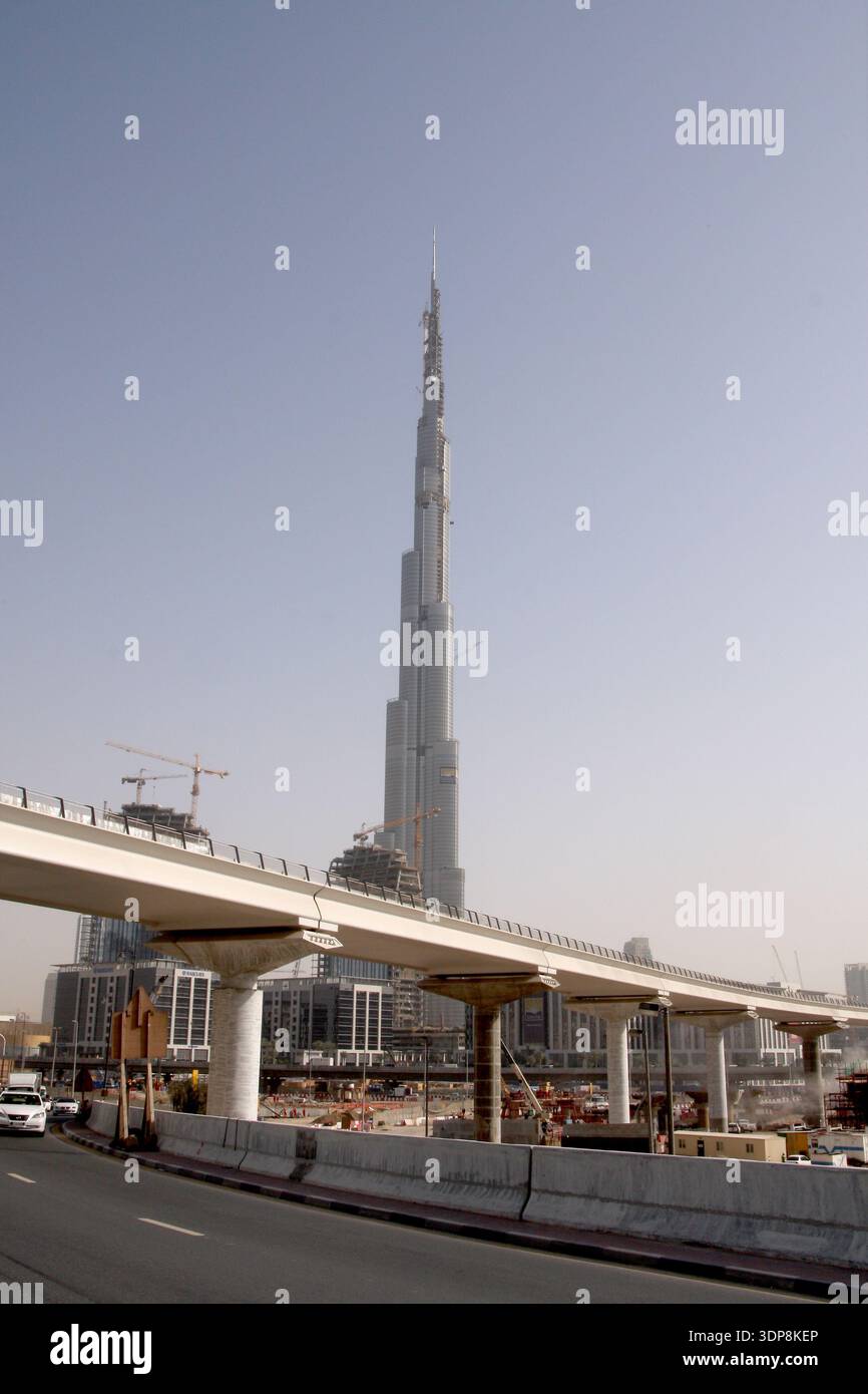 L'iconica torre Burj Khalifa si erge maestosa dietro un cavalcavia sopraelevato in cemento curvo nel centro di Dubai sotto un cielo sereno. Foto Stock