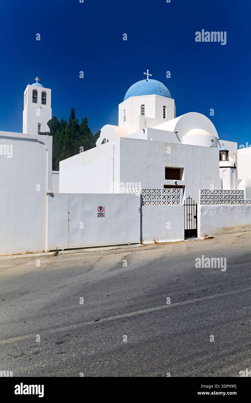 Una tradizionale chiesa greco-ortodossa bianca con una cupola blu e un campanile sotto un cielo limpido, caratteristica della splendida architettura dell'isola greca Foto Stock