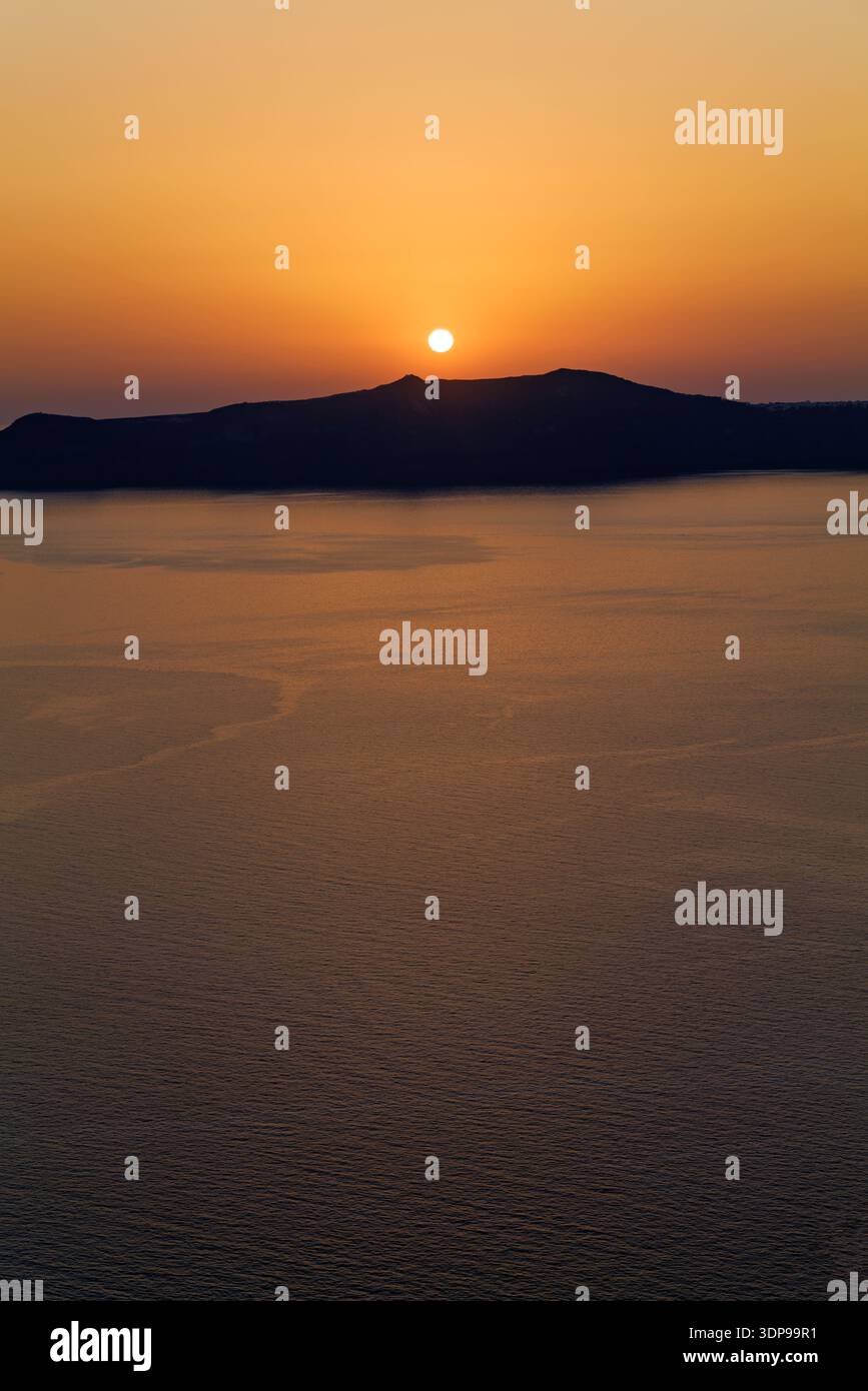 Un vibrante tramonto arancione sul Mar Egeo, con il sole che si immerge dietro una lontana sagoma dell'isola a Santorini, in Grecia Foto Stock