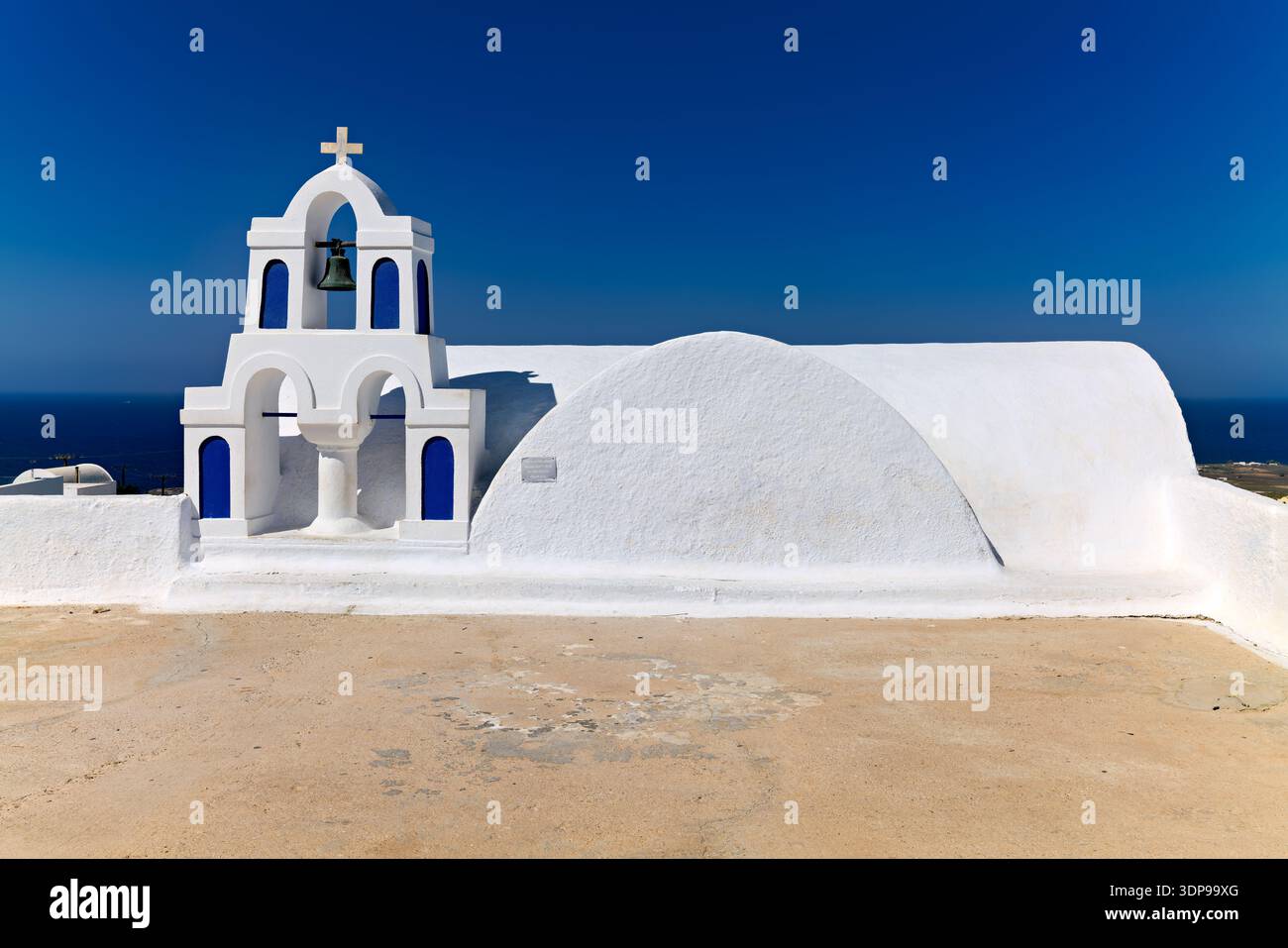 Una tradizionale chiesa greco-ortodossa bianca con un campanile e accenti blu sotto un cielo azzurro, che si affaccia sul Mar Egeo. Un luogo sacro su un GRE Foto Stock