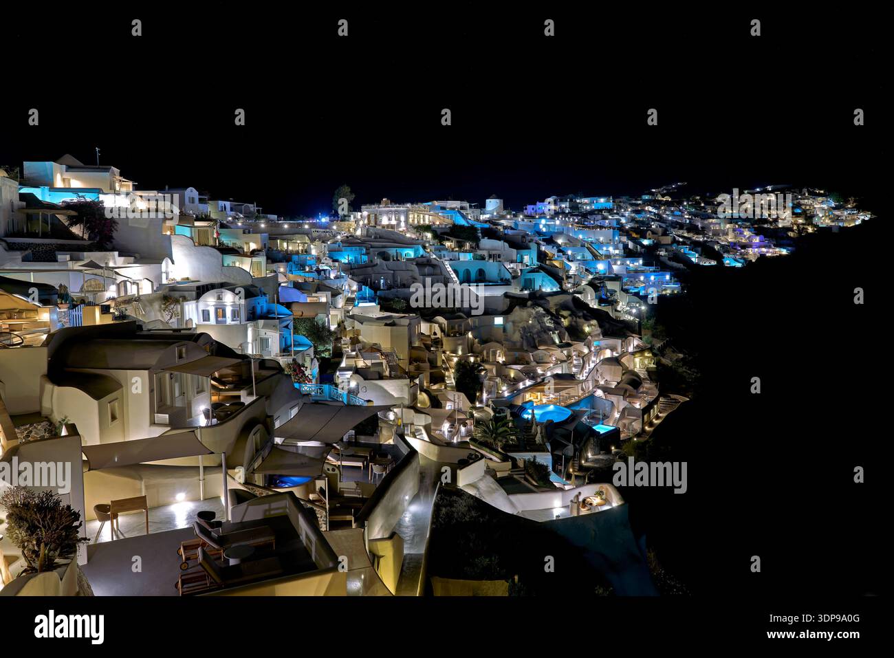 Una splendida vista notturna del villaggio illuminato sulla scogliera di Oia, Santorini, Grecia, che mostra i suoi iconici edifici bianchi e accenti blu. Foto Stock