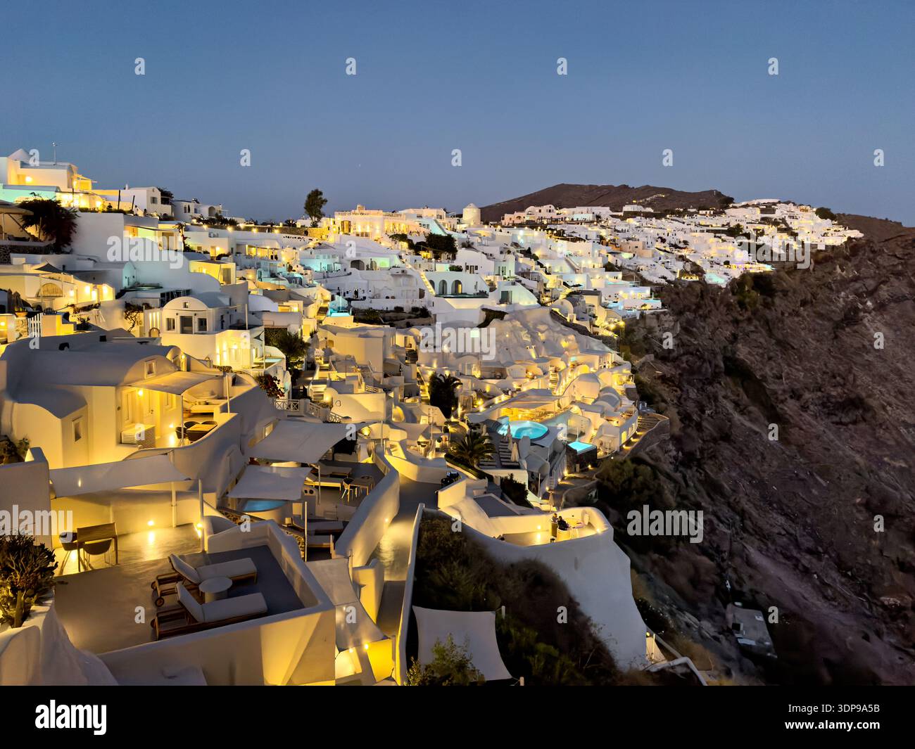 Santorini, Grecia: Gli edifici dipinti di bianco brillano al crepuscolo, mostrando l'iconica architettura sulla scogliera e l'atmosfera invitante per i visitatori. Foto Stock
