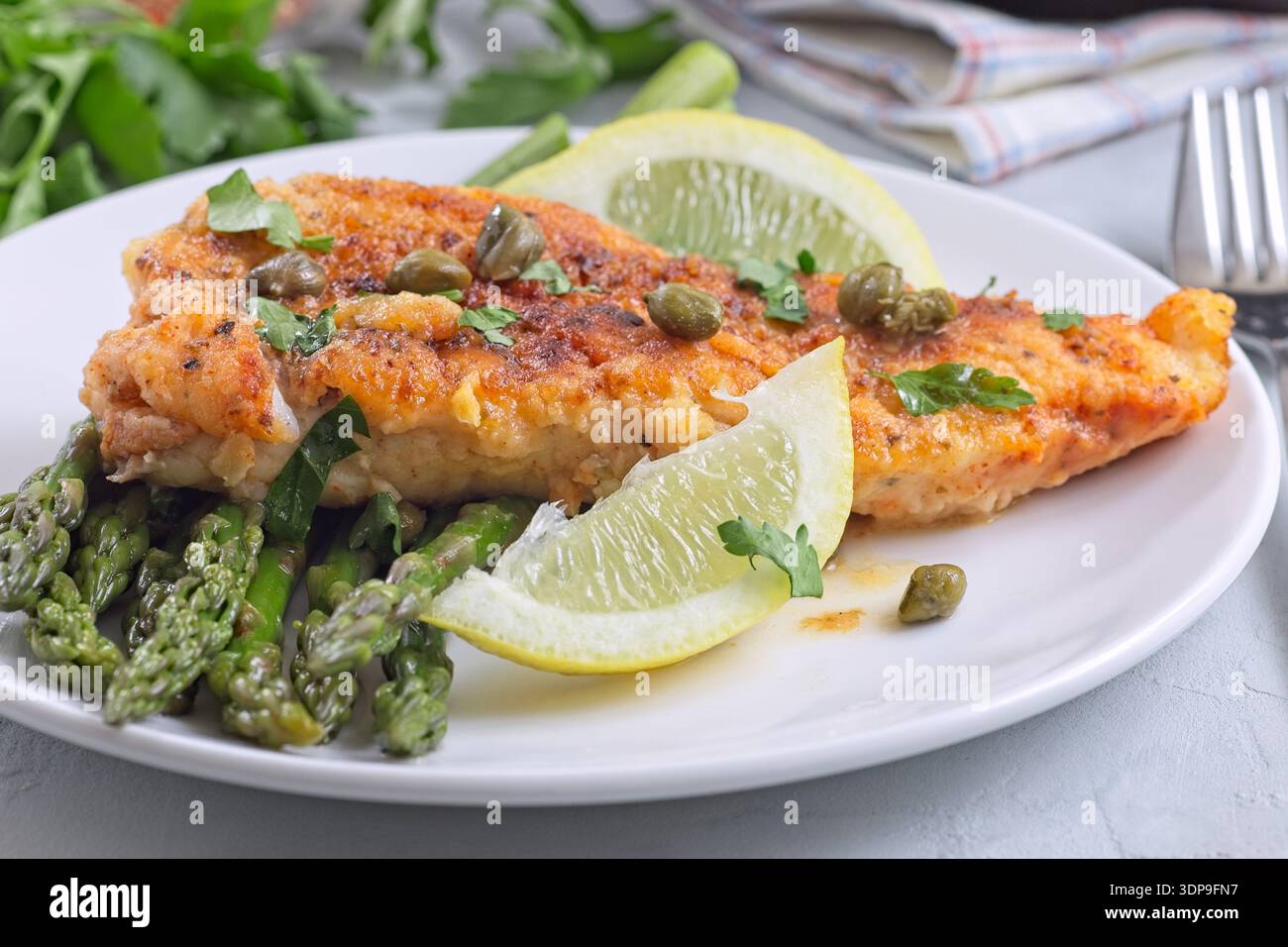 Piccata di pesce di eglefino, filetto di pesce pastella con capperi e spicchi di limone, servito con asparagi, pasto sano e saporito, orizzontale Foto Stock