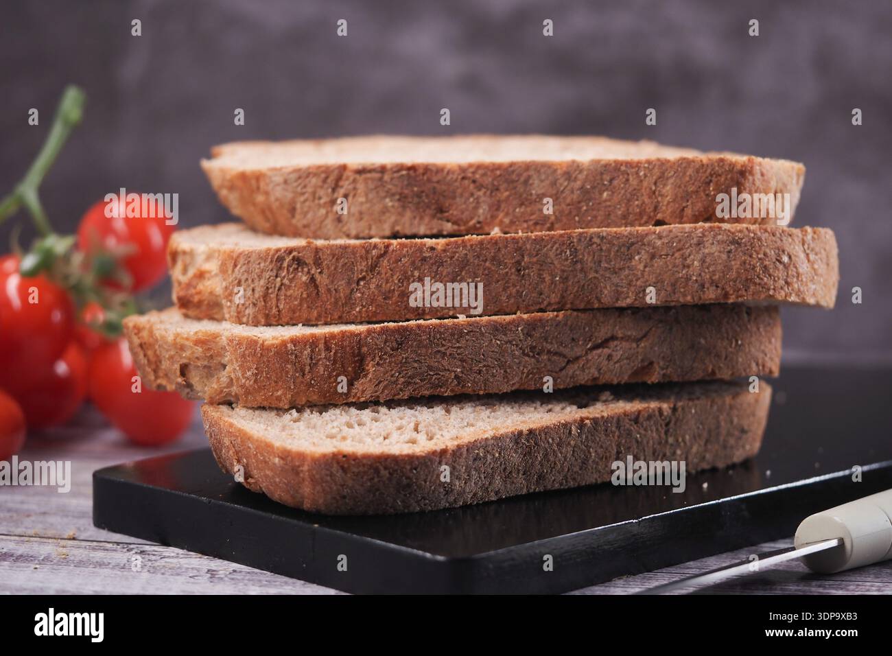 Fette fresche di pane integrale su un tagliere nero Foto Stock