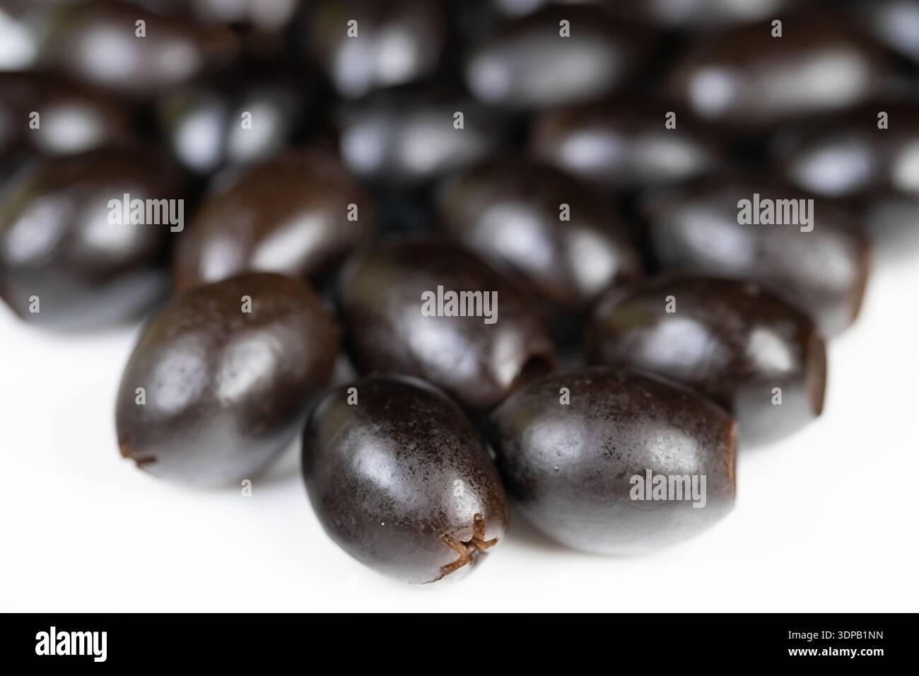 Primo piano di olive nere lucide su sfondo bianco, profondità di campo bassa, consistenza della pelle liscia, sottile lucentezza dell'olio, illuminazione da studio a contrasto elevato, cucina Foto Stock