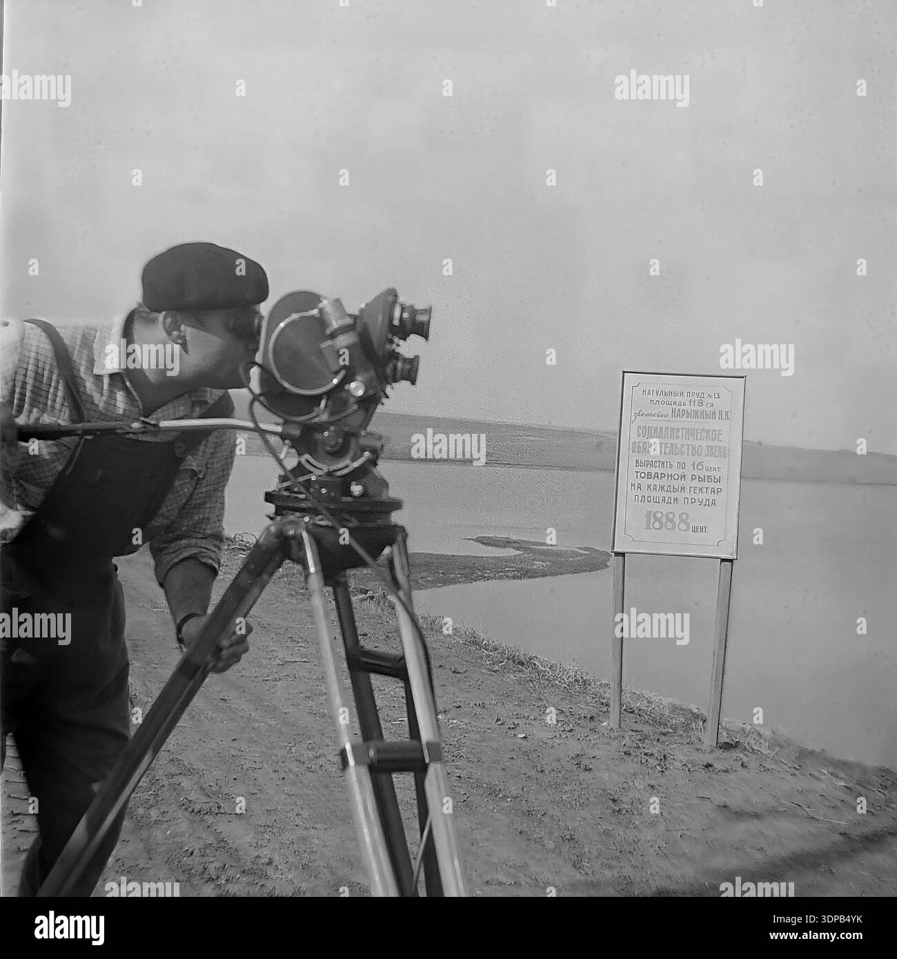 Distretto di Slavyansk, regione di Donetsk, Ucraina, URSS. Tra la fine degli anni '1960 e i primi anni '1970 Un cameraman filma un documentario sui risultati dell'allevamento ittico Donrybkombinat. Accanto alla videocamera professionale su un treppiede c'è una bacheca informativa che illustra gli "obblighi socialisti" del team guidato da N.K. Naryzhny. L'obiettivo è quello di raccogliere 1888 centimetri di pesce dal laghetto da ingrasso n. 13 con una superficie di 118 ettari. Sullo sfondo, il serbatoio è visibile. Un'autentica scena storica della gloria del lavoro sovietico e della propaganda nel pacifico Donbas prima della guerra. Foto Stock