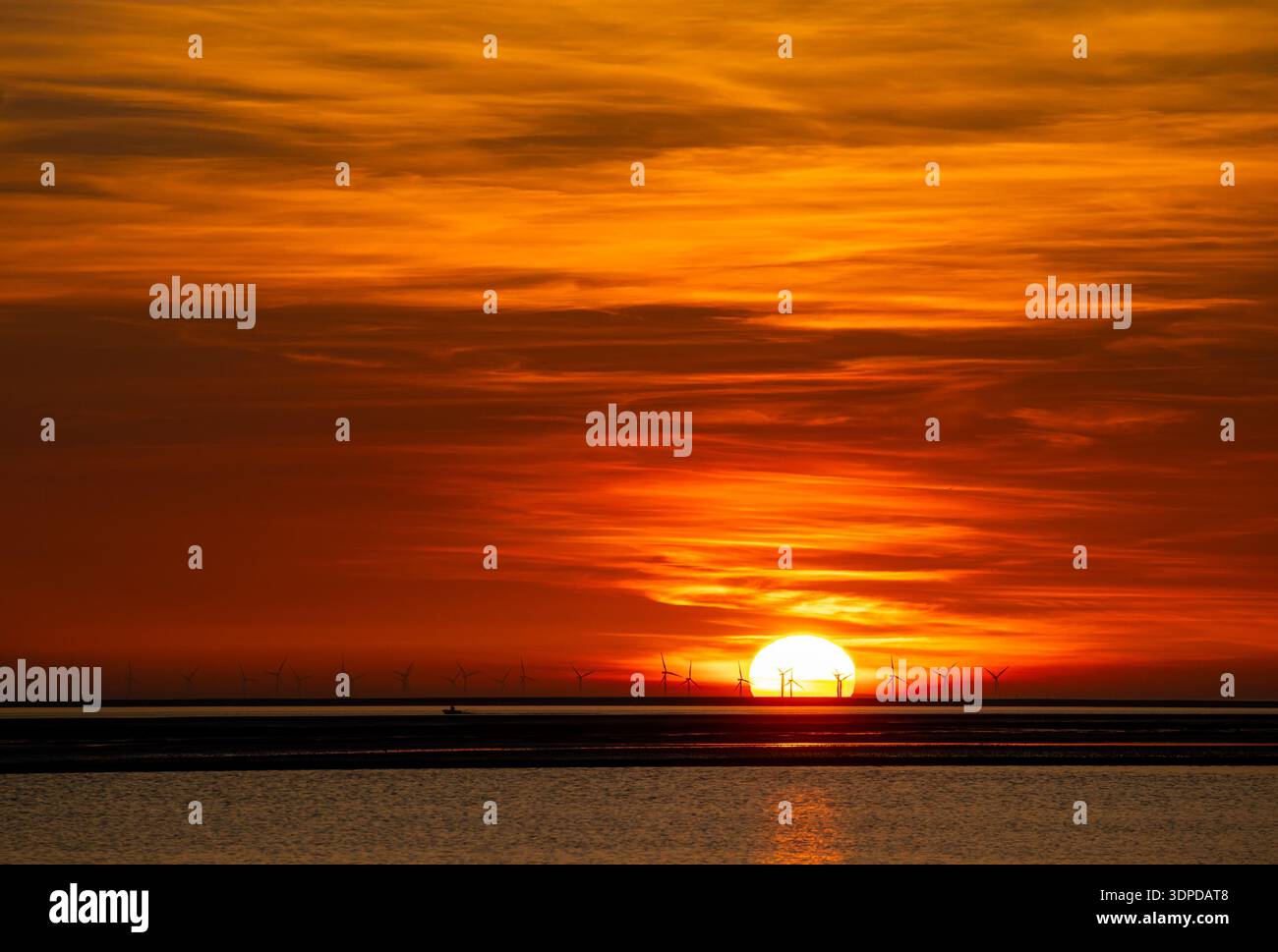 Tramonto vibrante su un paesaggio costiero dove un lontano parco eolico si staglia contro un cielo brillante e ardente Foto Stock