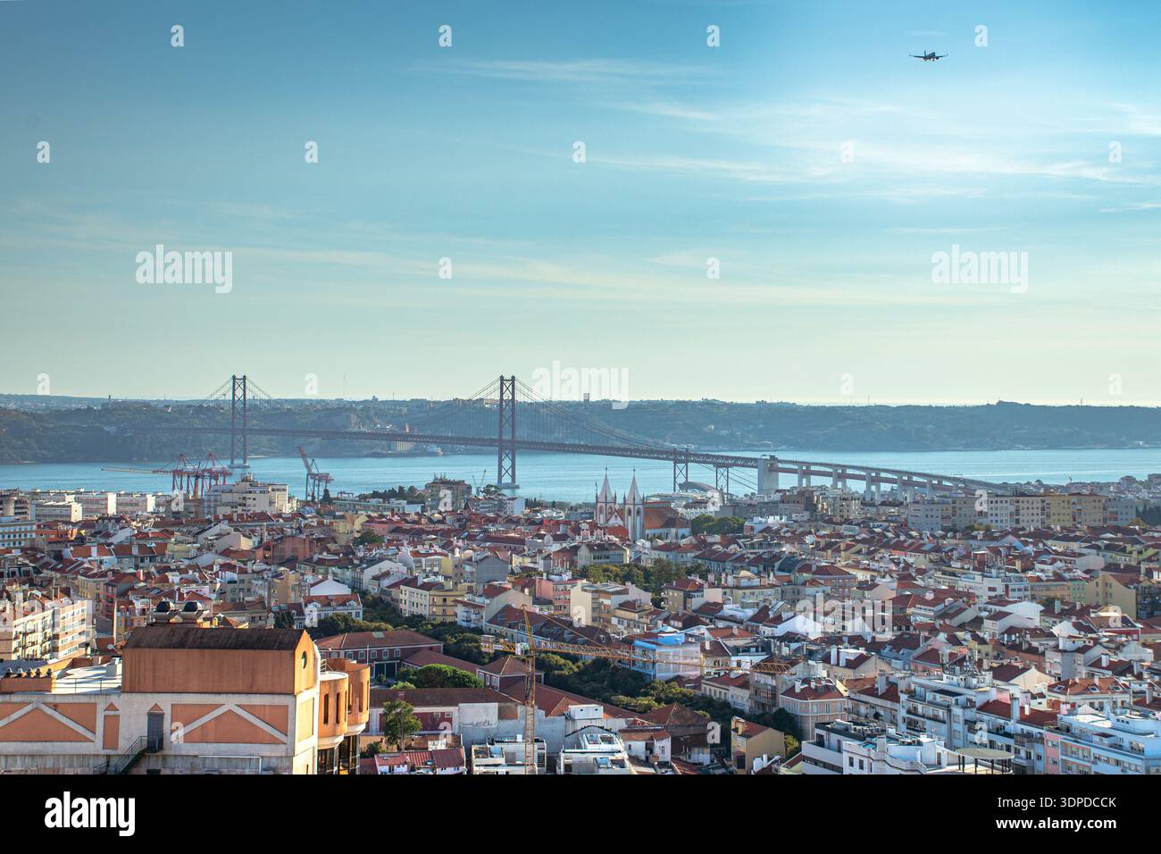 Vista panoramica di una città storica con tetti di tegole rosse che si affacciano su un ampio fiume. Un grande ponte sospeso attraversa l'acqua a Lisbona, in Portogallo. Foto Stock