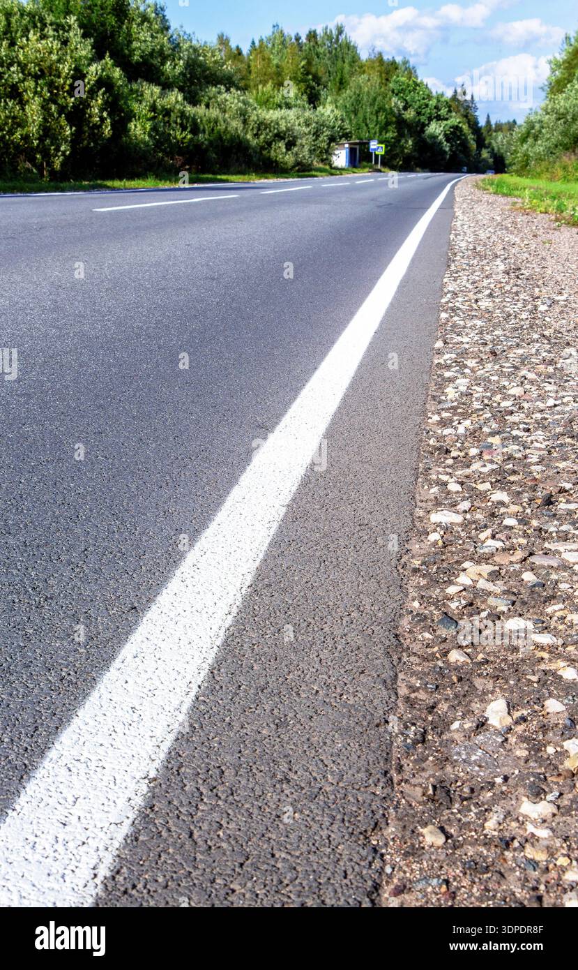 Una linea bianca continua che segna su una strada asfaltata in campagna in estate Foto Stock