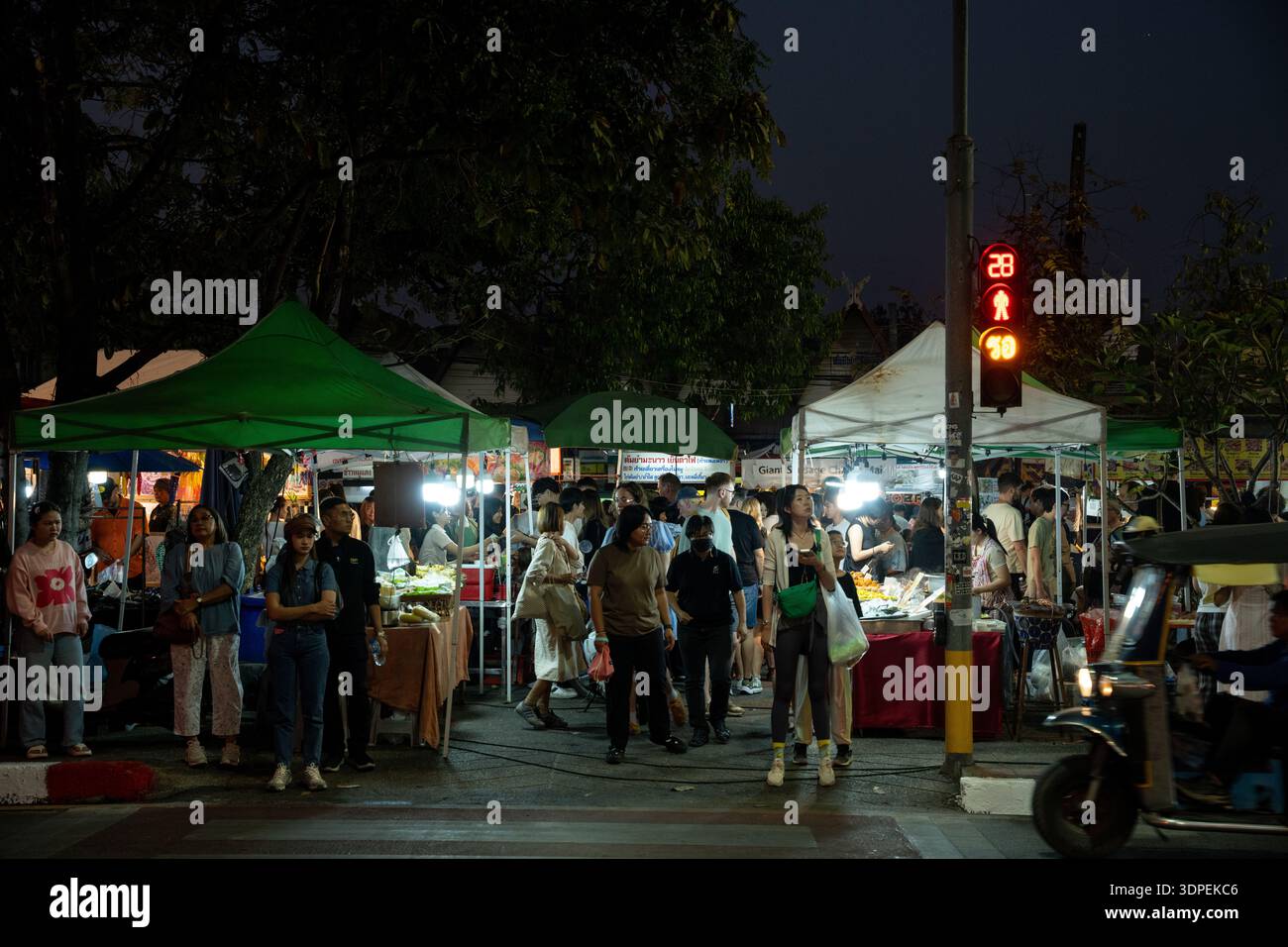 Una folla di gente del posto e turisti esplora un vivace mercato di Street food di notte a Chiang mai, Thailandia. La scena è illuminata dalla luce di stallo Foto Stock