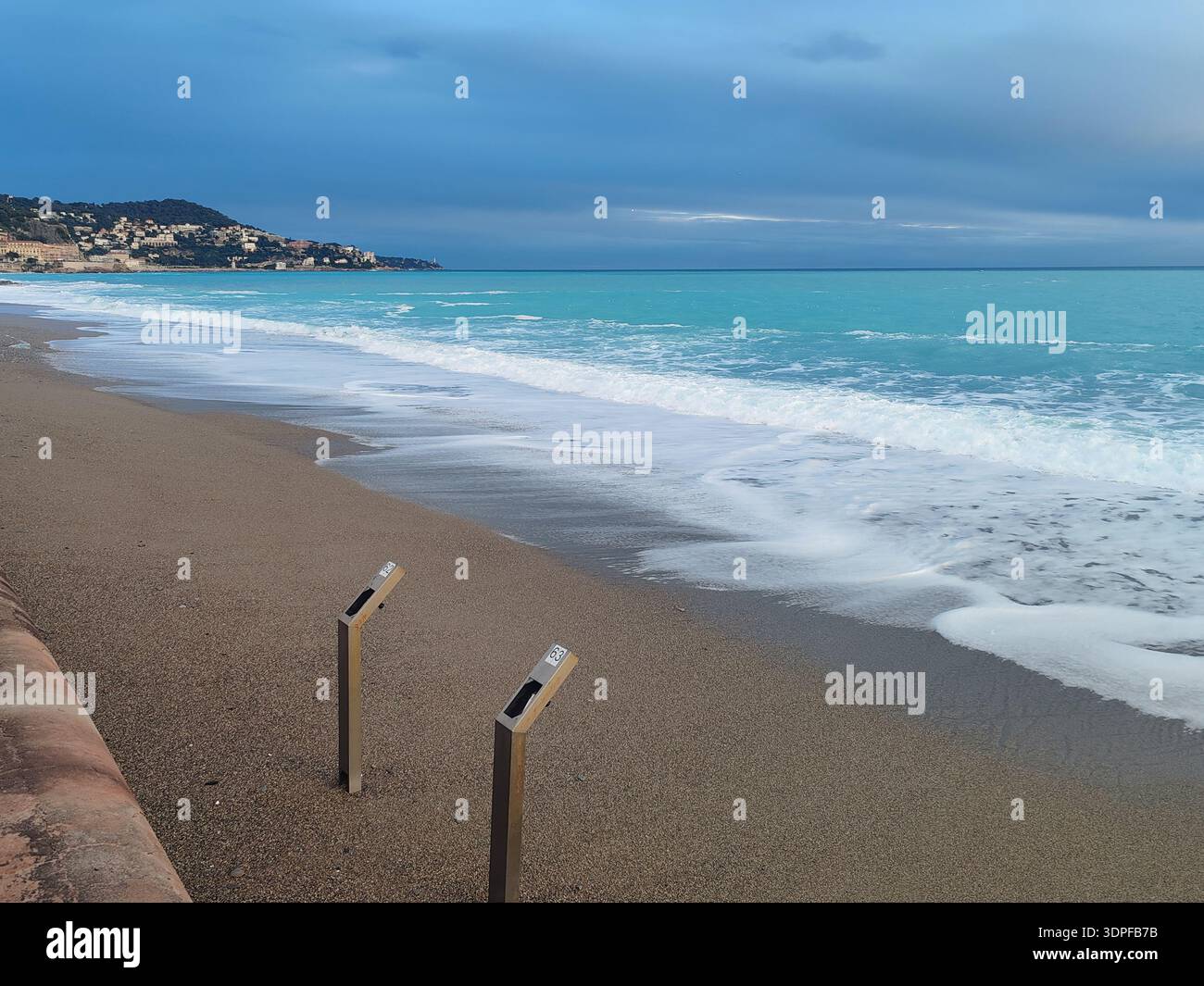 Mare Mediterraneo serale dopo la tempesta con docce in spiaggia metà sepolte nella sabbia bagnata dalle forti onde della Costa Azzurra Foto Stock