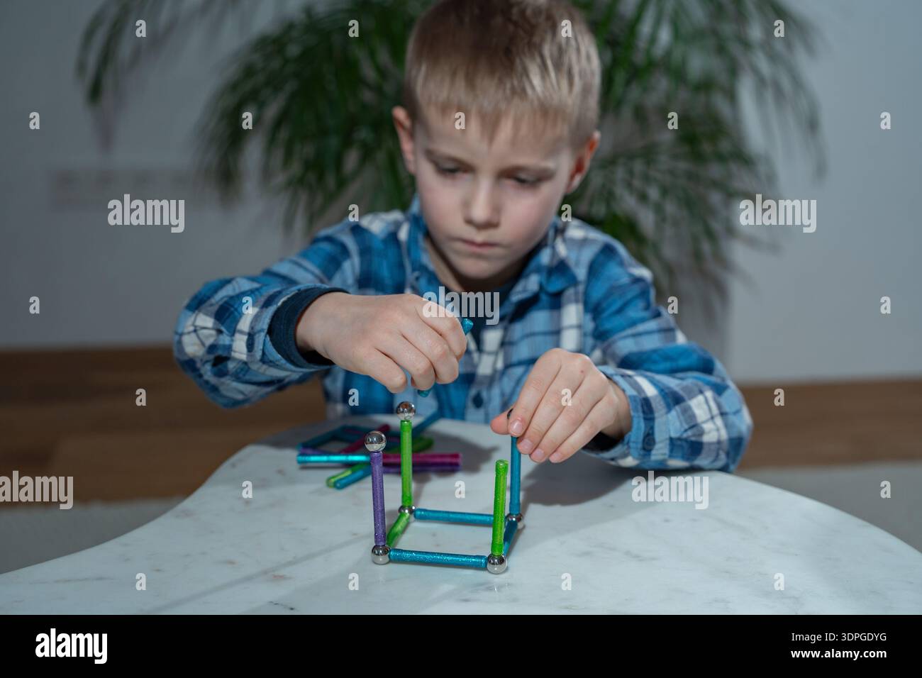 Bambino impegnato in un'attività pratica di apprendimento a casa utilizzando un colorato set di costruzioni magnetiche. Concetto di Homeschooling, crescita cognitiva, creatività Foto Stock