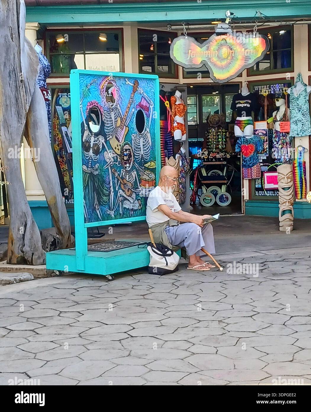 Un uomo anziano che legge un giornale davanti a un colorato negozio di souvenir tropicali a Lahaina Maui, Hawaii. Foto Stock