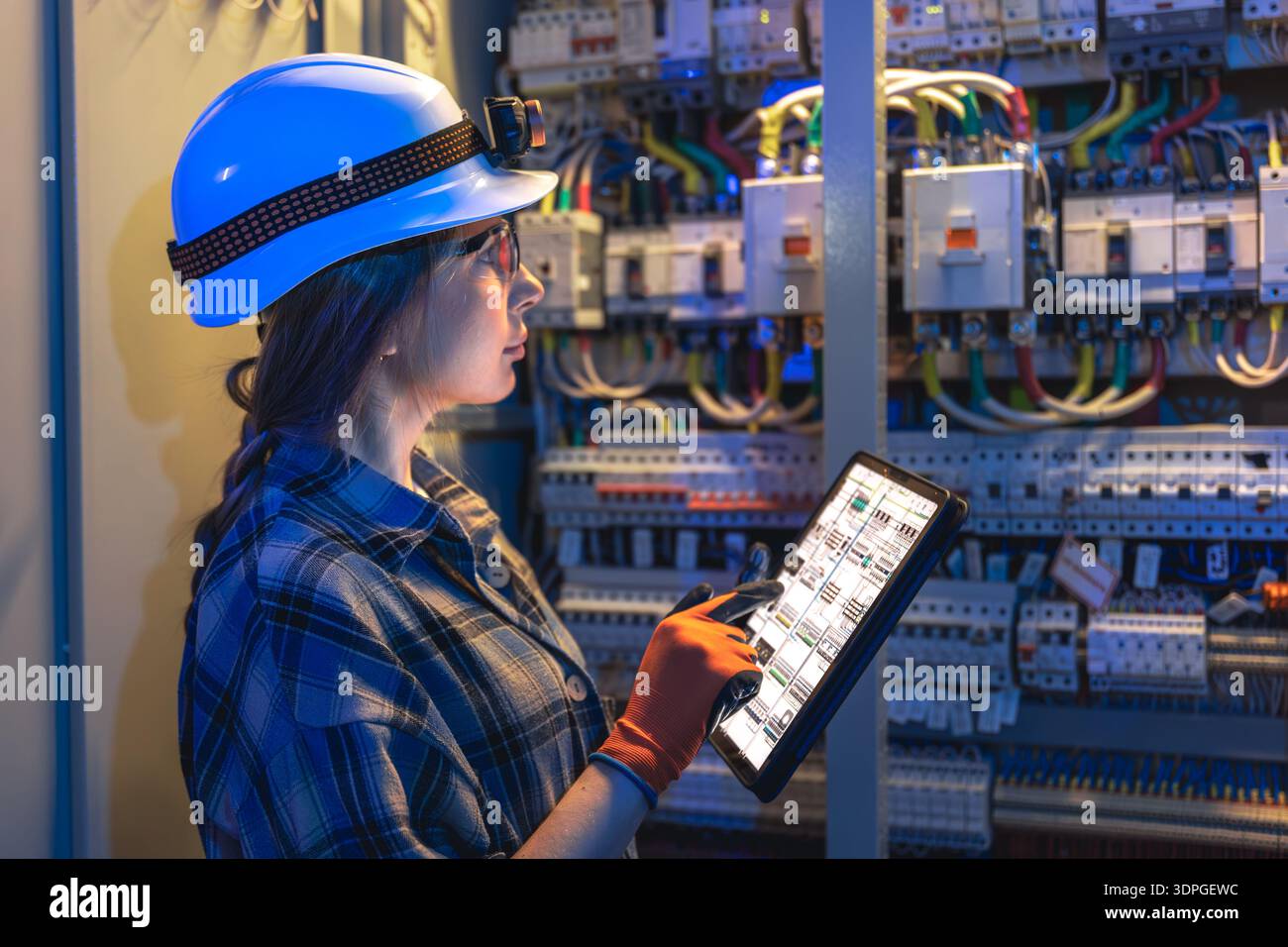 Una donna elettricista convalida i quadri di comando con un tablet. Controllo digitale. Foto Stock