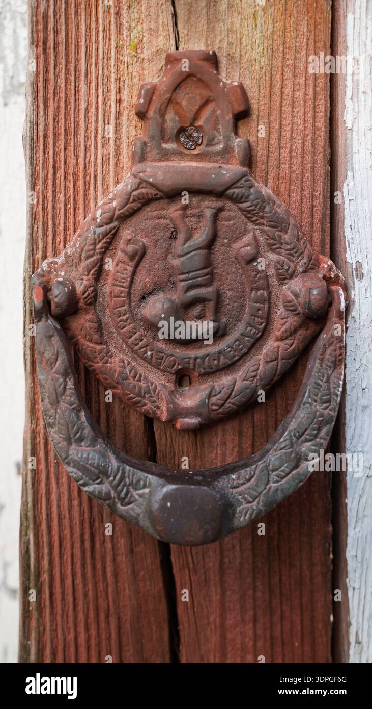 Primo piano di una porta in ghisa antica arrugginita con rilievo ornato su una porta in legno rosso testurizzato. Foto Stock
