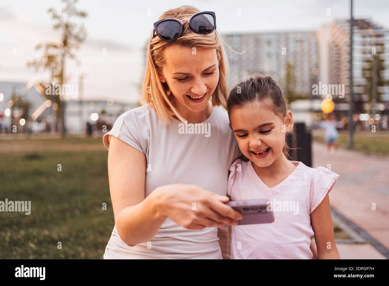 Madre e figlia guardano lo smartphone e sorridono nel parco Foto Stock