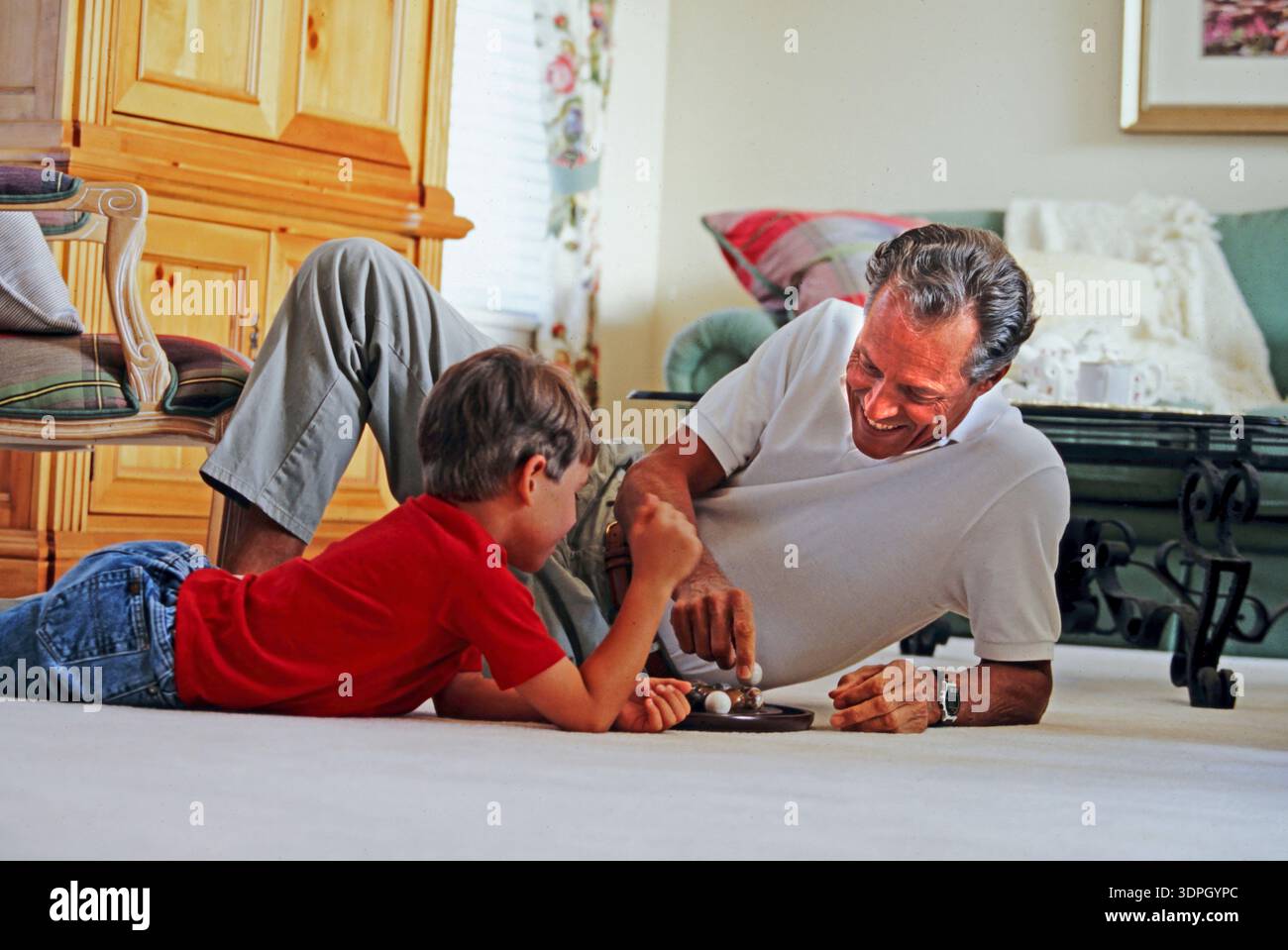 Un nonno e un nipote sono sul pavimento a divertirsi insieme. Il padre del quando sorride mentre il ragazzo si concentra sul gioco di fronte a loro. La stanza h Foto Stock