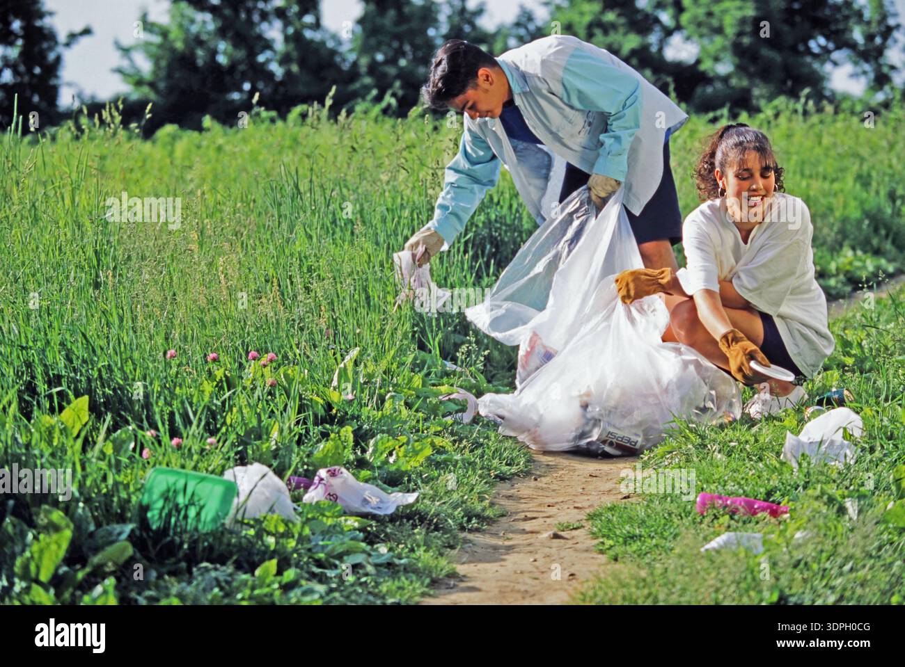 Due giovani volontari che svolgono il servizio di comunità raccolgono rifiuti dal suolo in un'area erbosa, lavorando insieme per ripulire l'ambiente. Loro noi sì sì sì no risposta Foto Stock