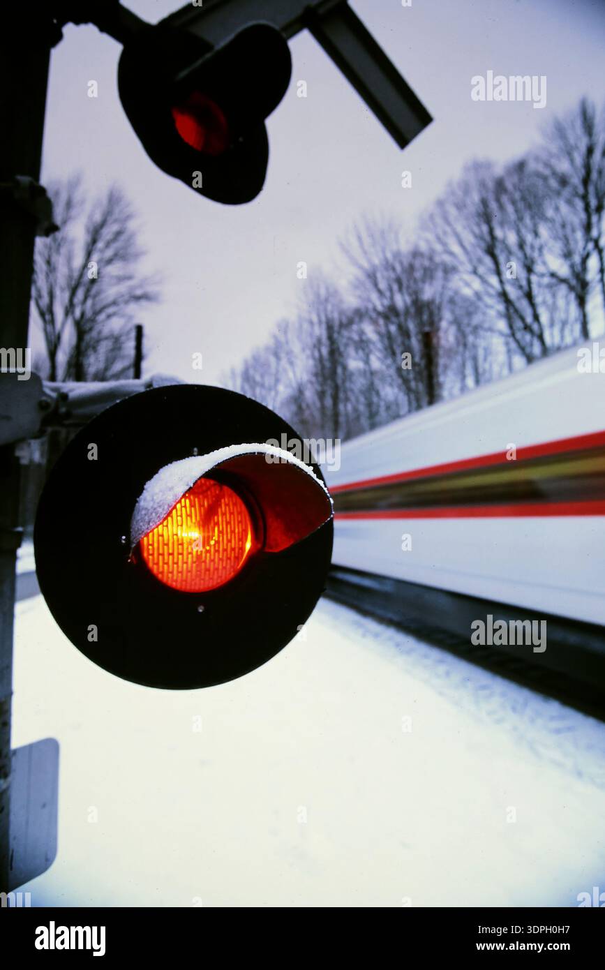 I segnali del treno mostrano un semaforo rosso mentre un treno attraversa un paesaggio innevato al crepuscolo vicino alla stazione in inverno Foto Stock